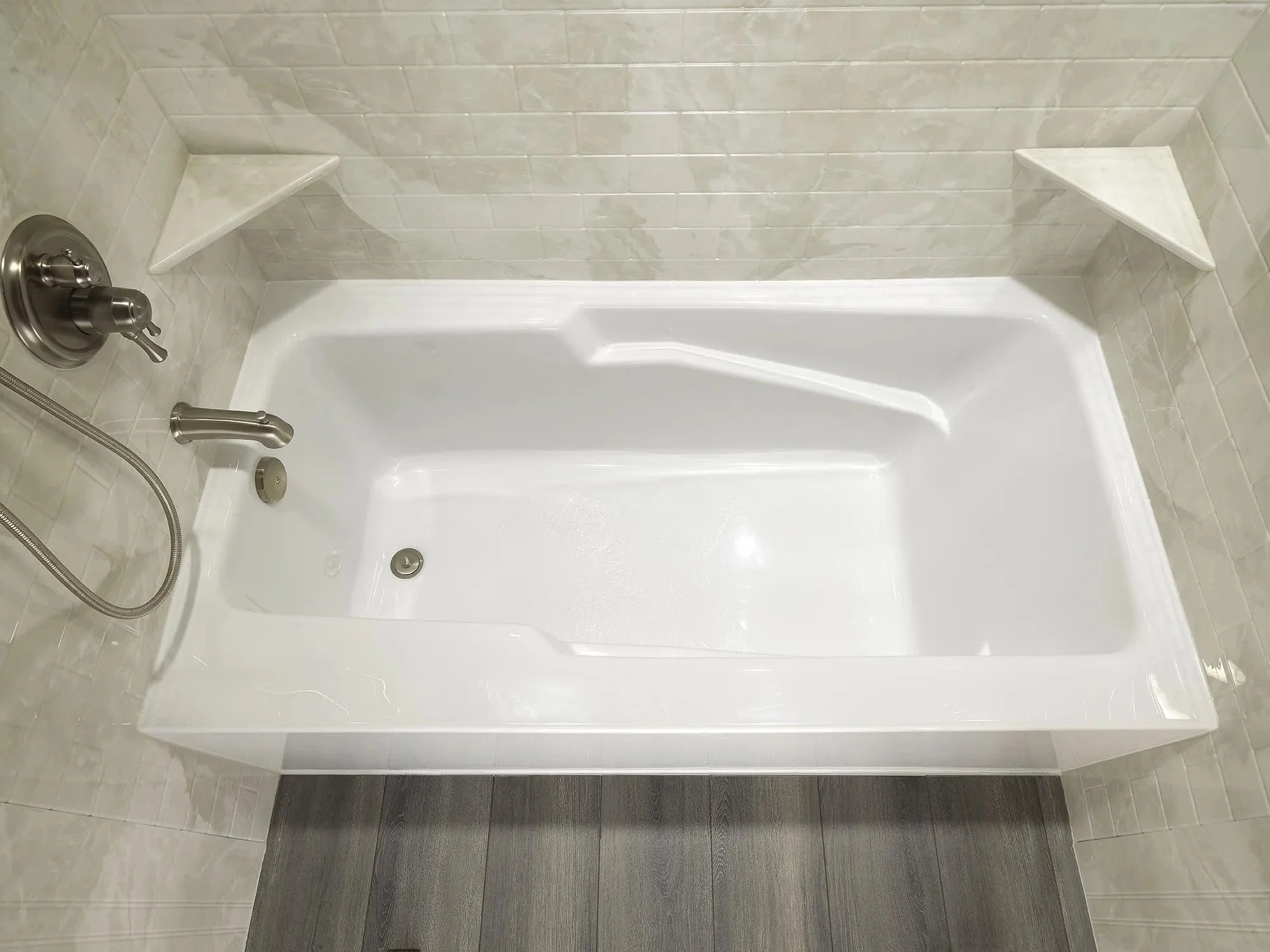 Empty white bathtub with a showerhead and brushed nickel fixtures in a tiled bathroom.