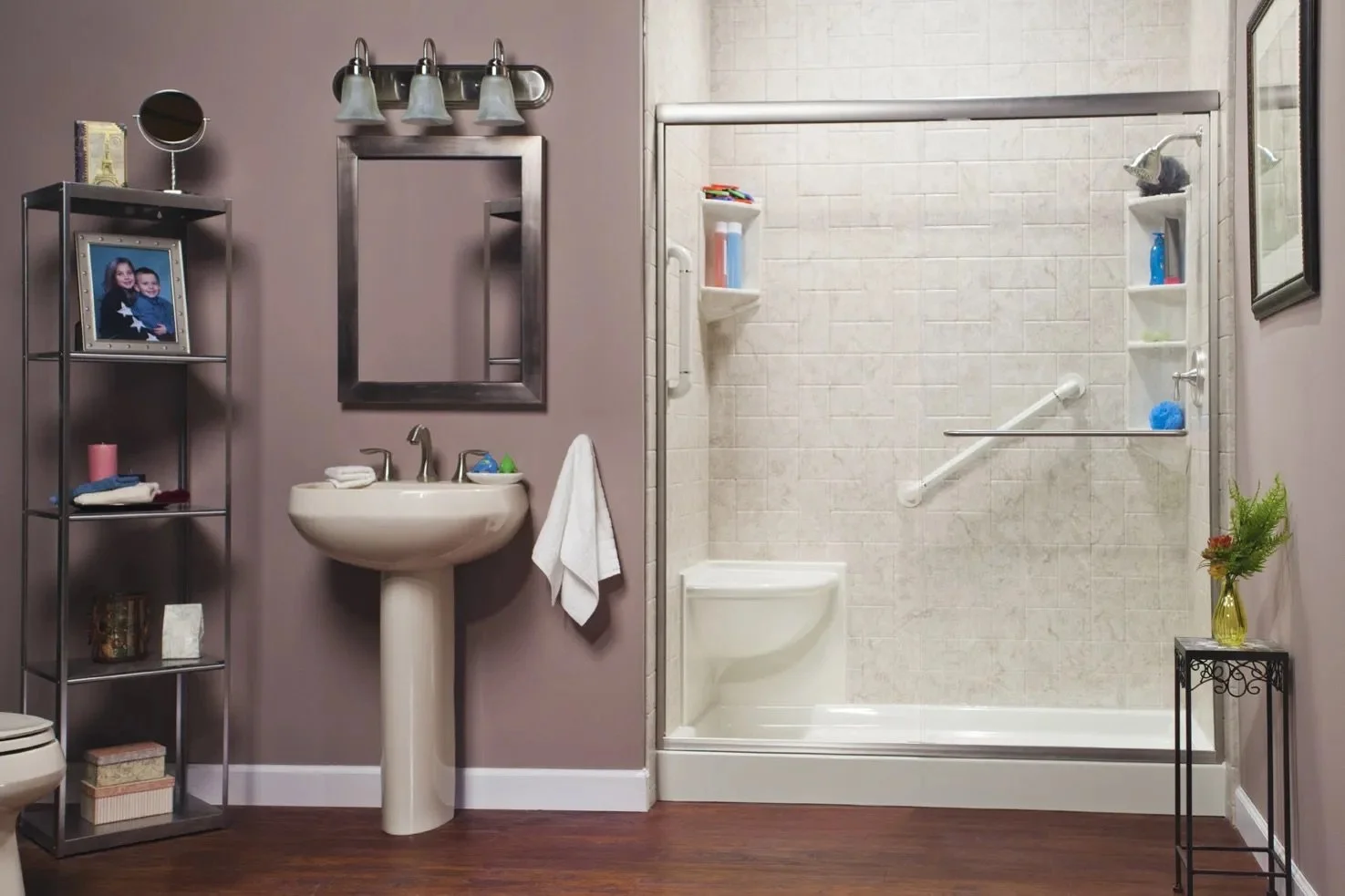 Bathroom with a shower stall, pedestal sink, mirror, and a metal shelving unit with framed photograph, towels, and decorative items.