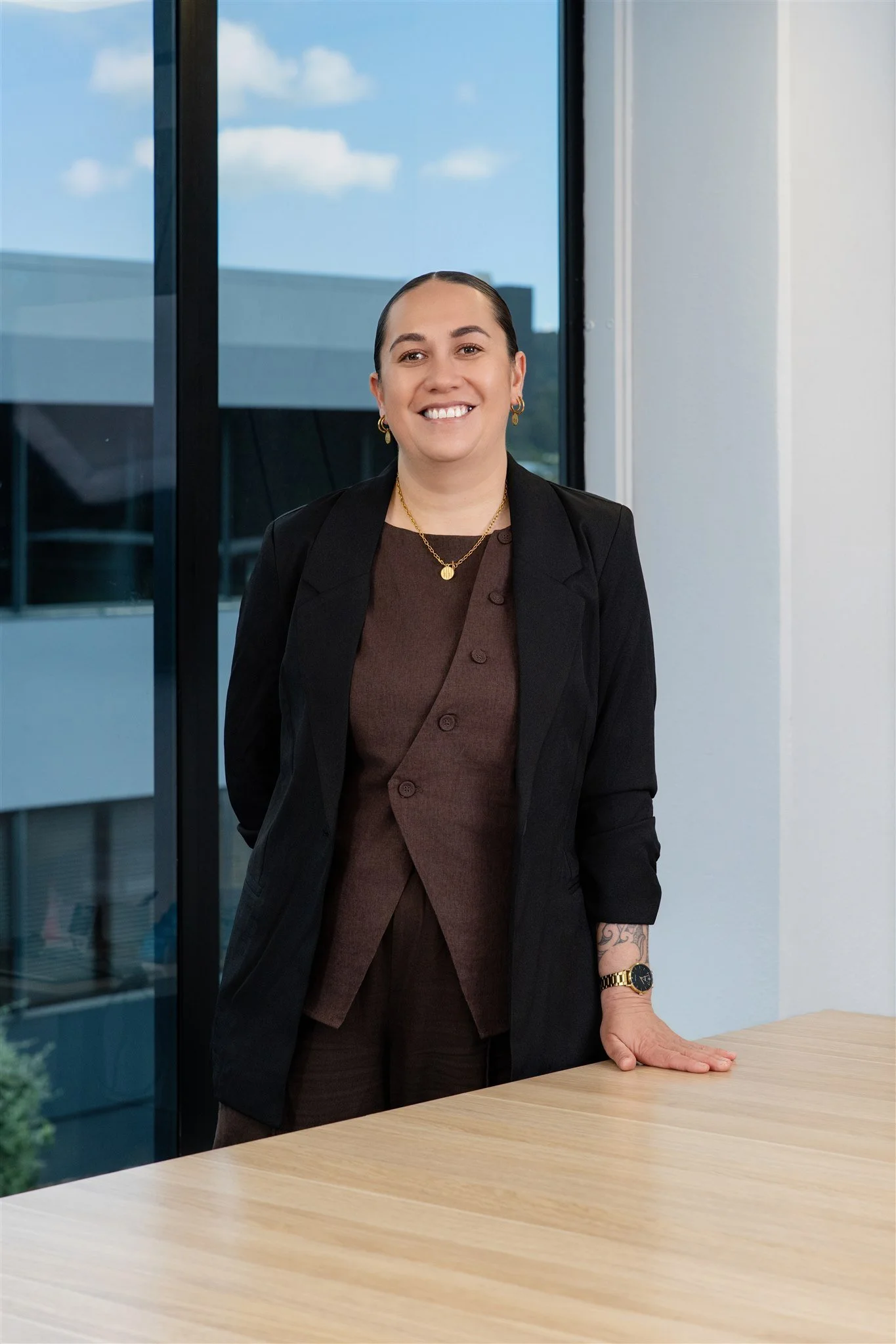 Businesswoman standing in an office near a window with a cityscape background, smiling at the camera.