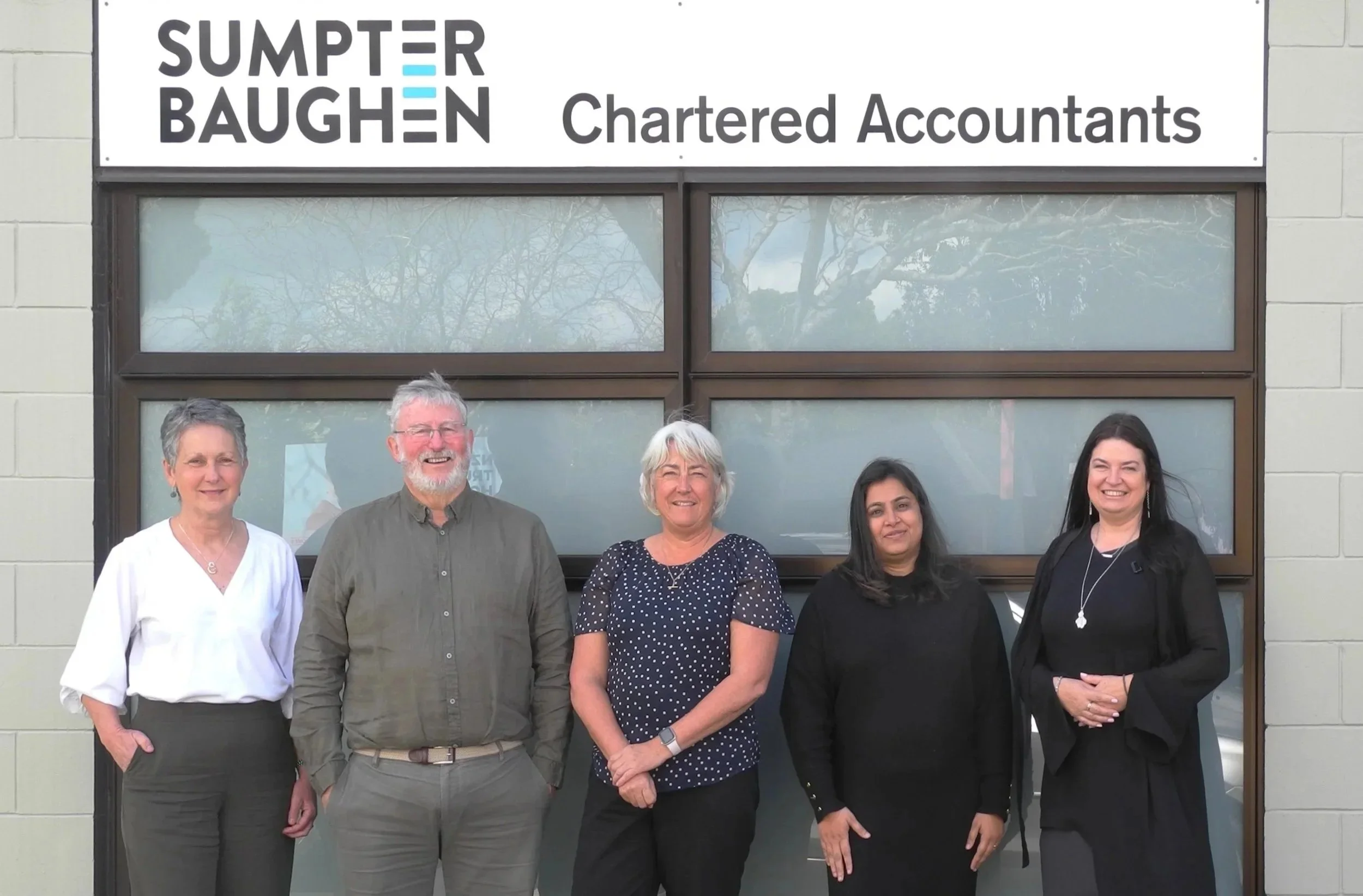 Group of five people standing in front of a building with a sign that reads 'Sumpter Baughen Chartered Accountants.'