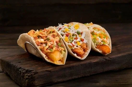 Three tacos filled with various ingredients on a wooden surface.