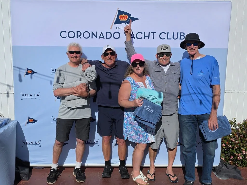 Photo of the regatta winners, four men and one woman smile for the camera. The logos of Coronado Yacht Club and Vela-LA are on the background.
