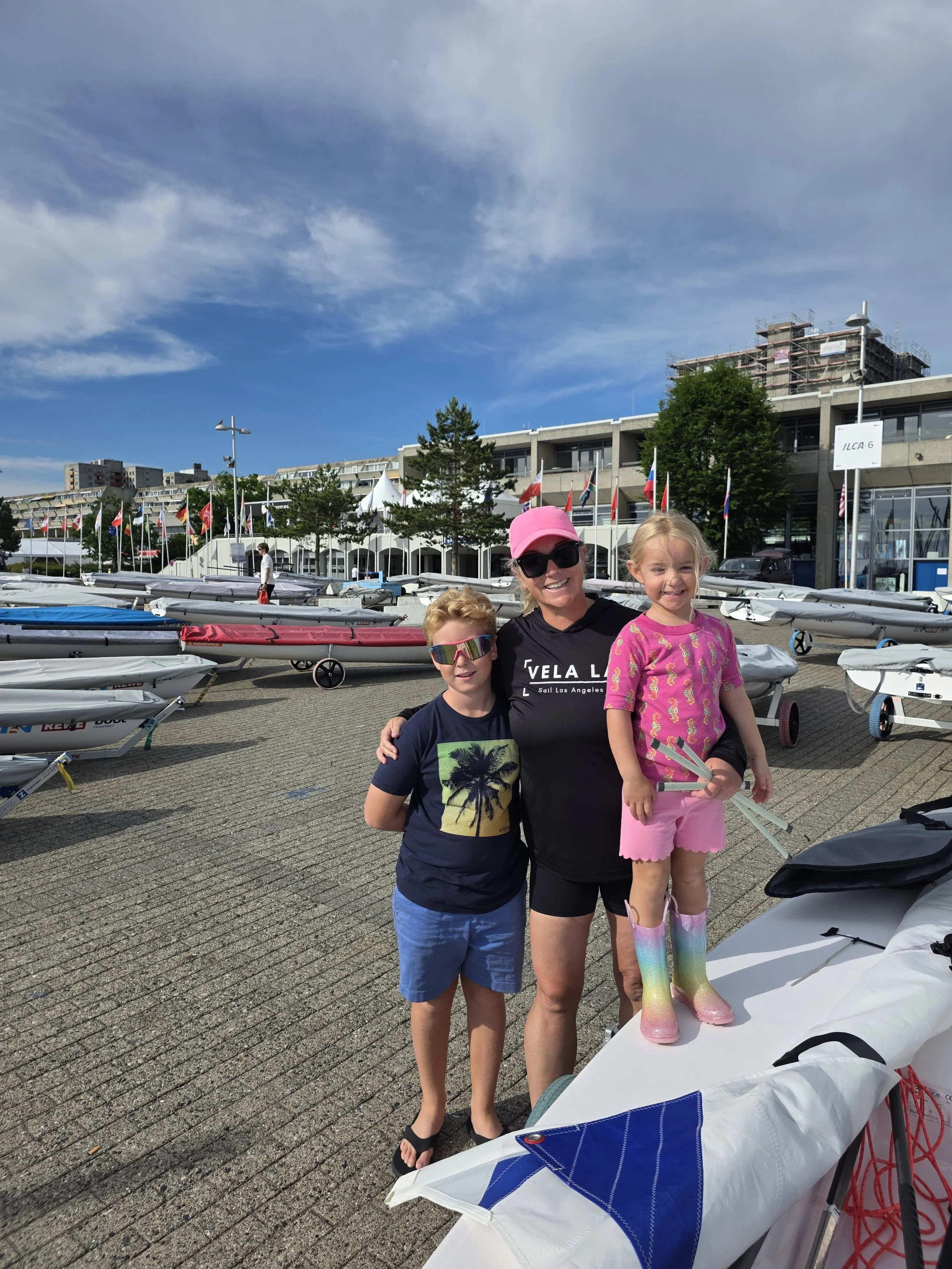 Lauren and her two children posing next to her Olympic class boat an ILCA 6 at Kieler Woche for the Sailing Grand Slam in June 2026