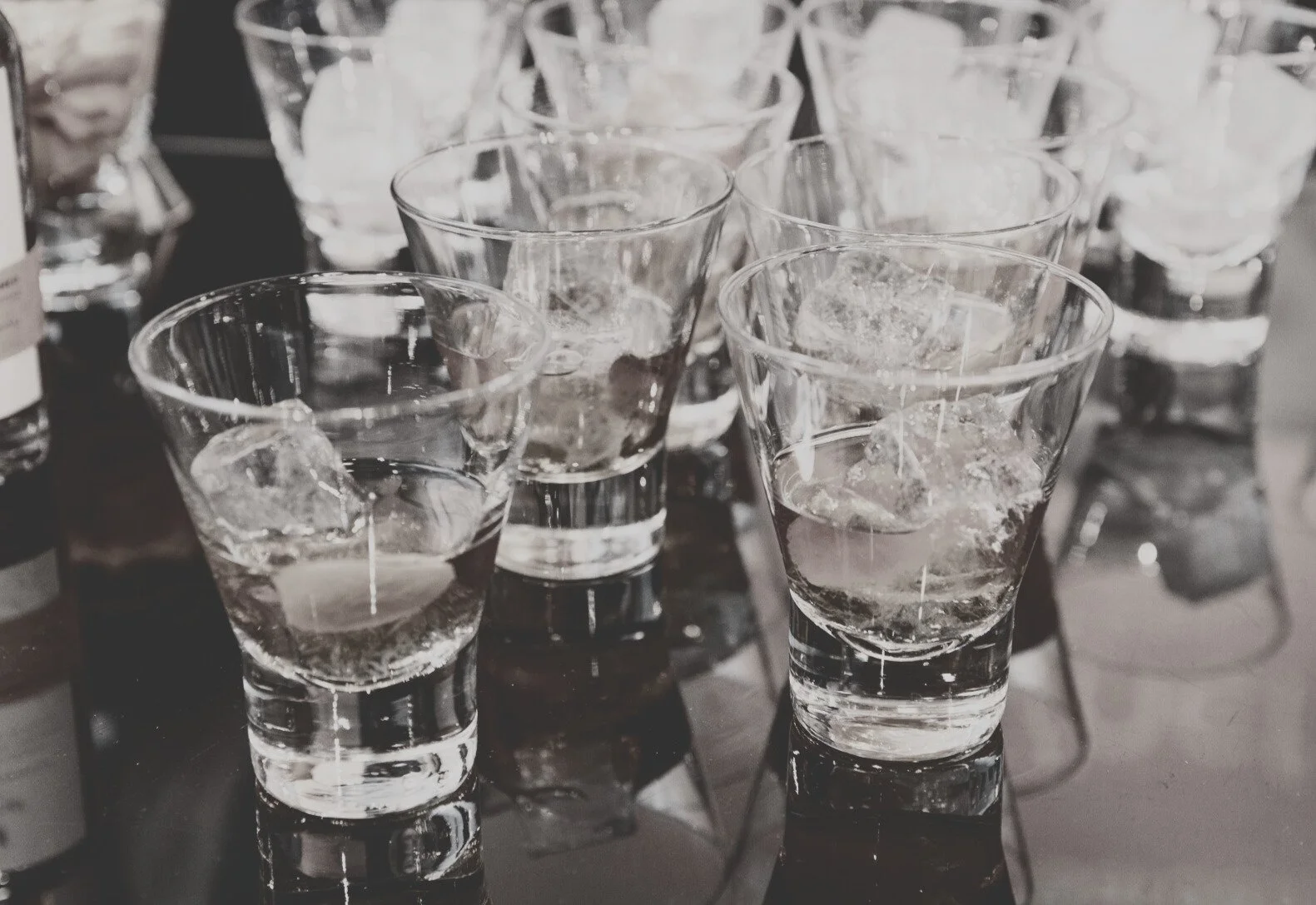 Multiple glasses filled with ice cubes and water, arranged on a reflective surface for a wedding.