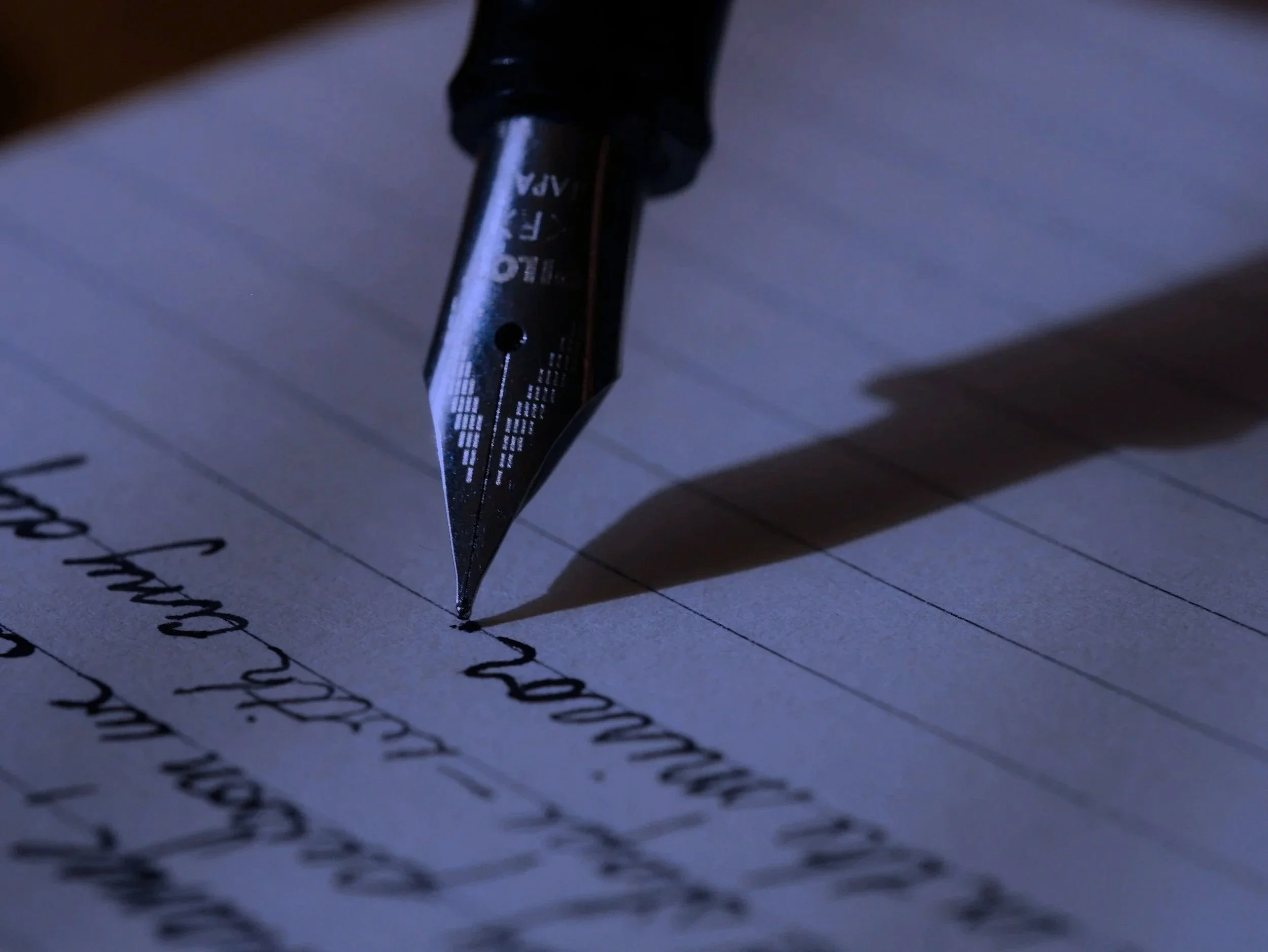 Close-up of a black fountain pen writing on lined paper with cursive handwriting.