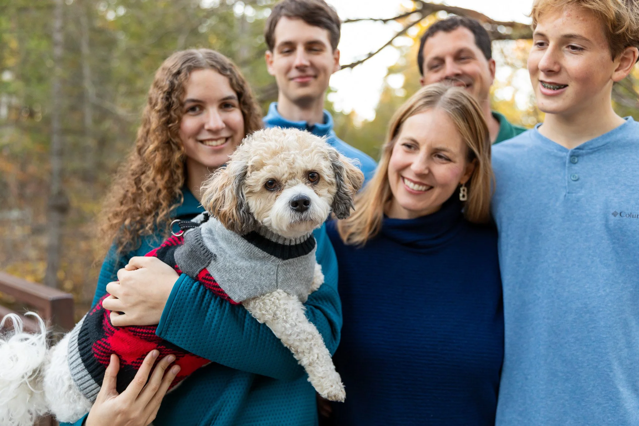 A group of five people and a dog outdoors in a park with autumn foliage.