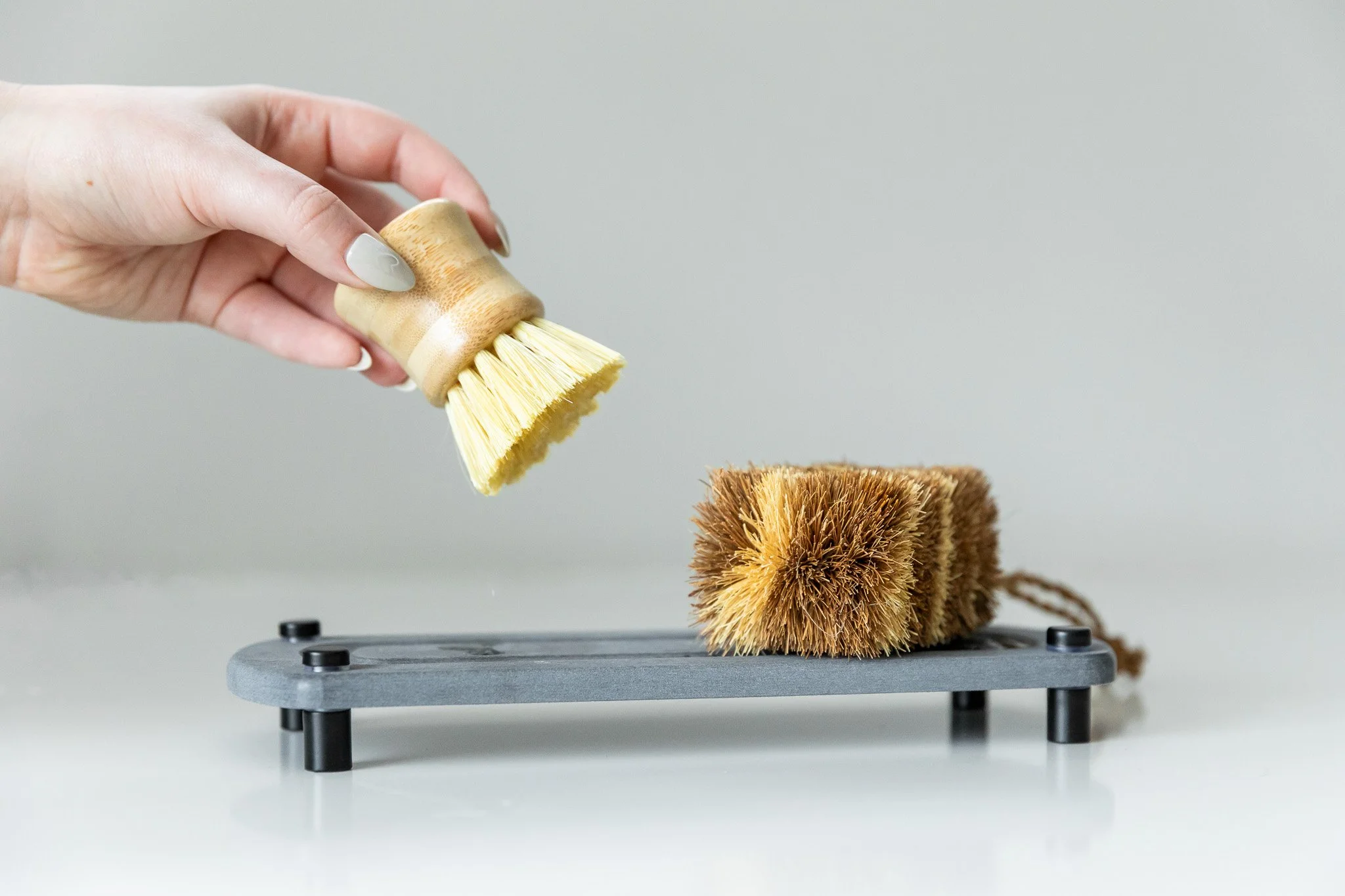 A hand holding a small brush wiping dust off a rectangular scratch brush on a gray surface.