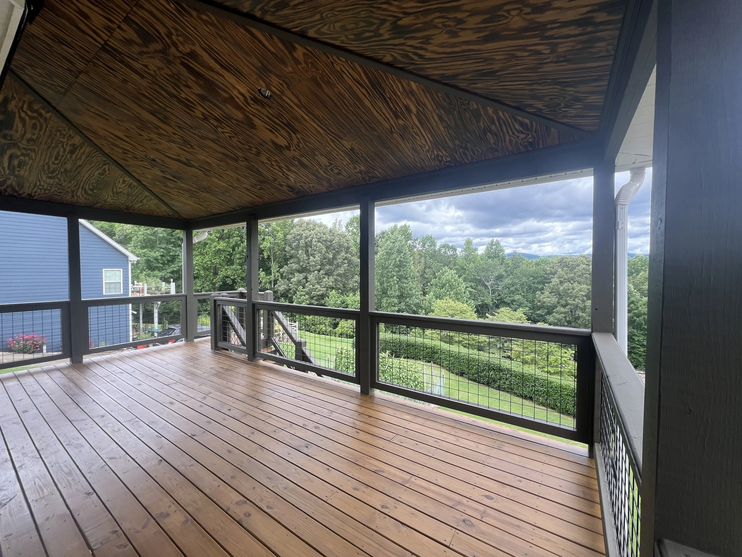 Empty porch with wooden floor and railing overlooking a lush green landscape and cloudy sky.