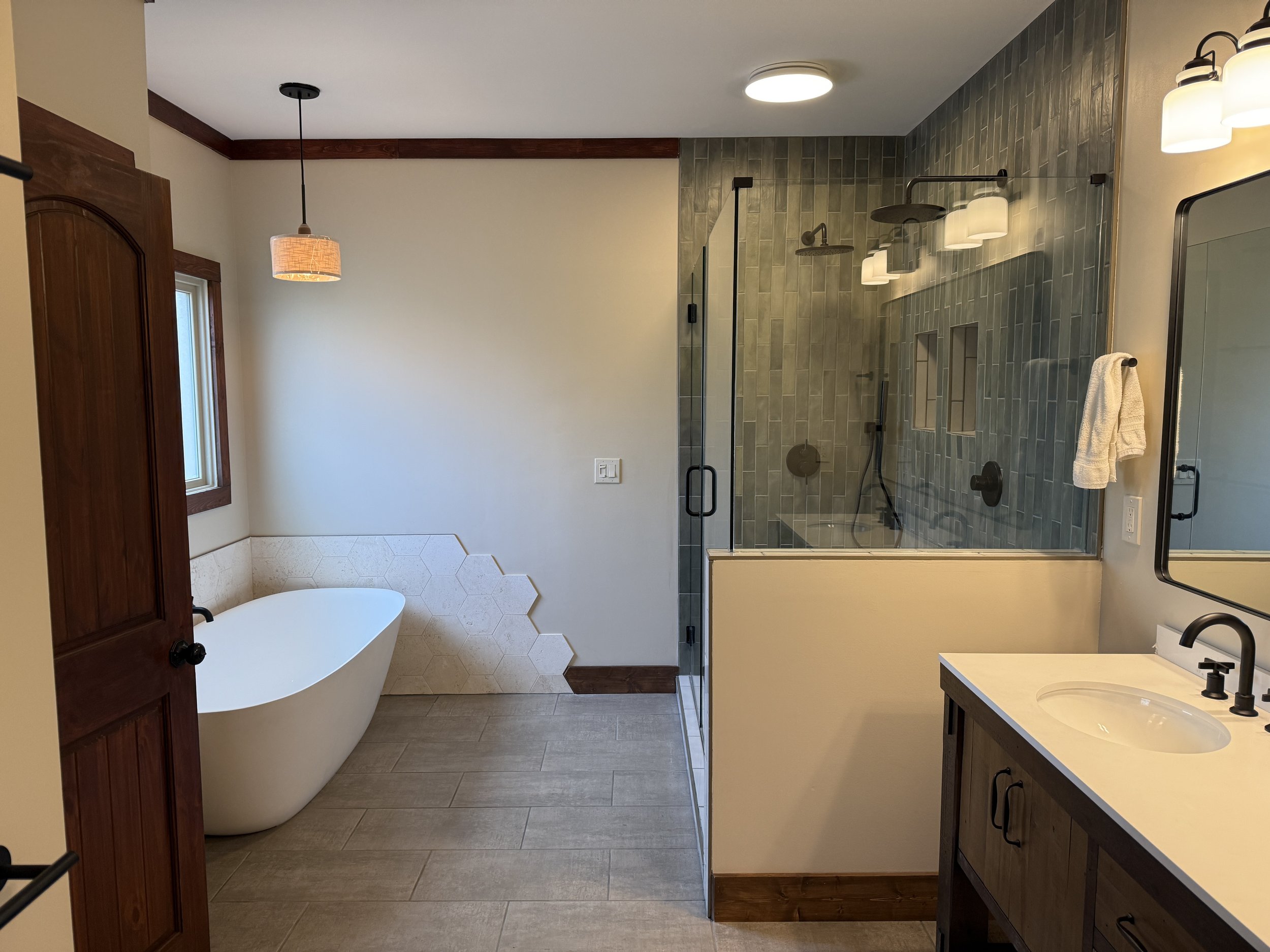 Modern bathroom with a walk-in shower, bathtub, vanity with sink, and wooden accents.