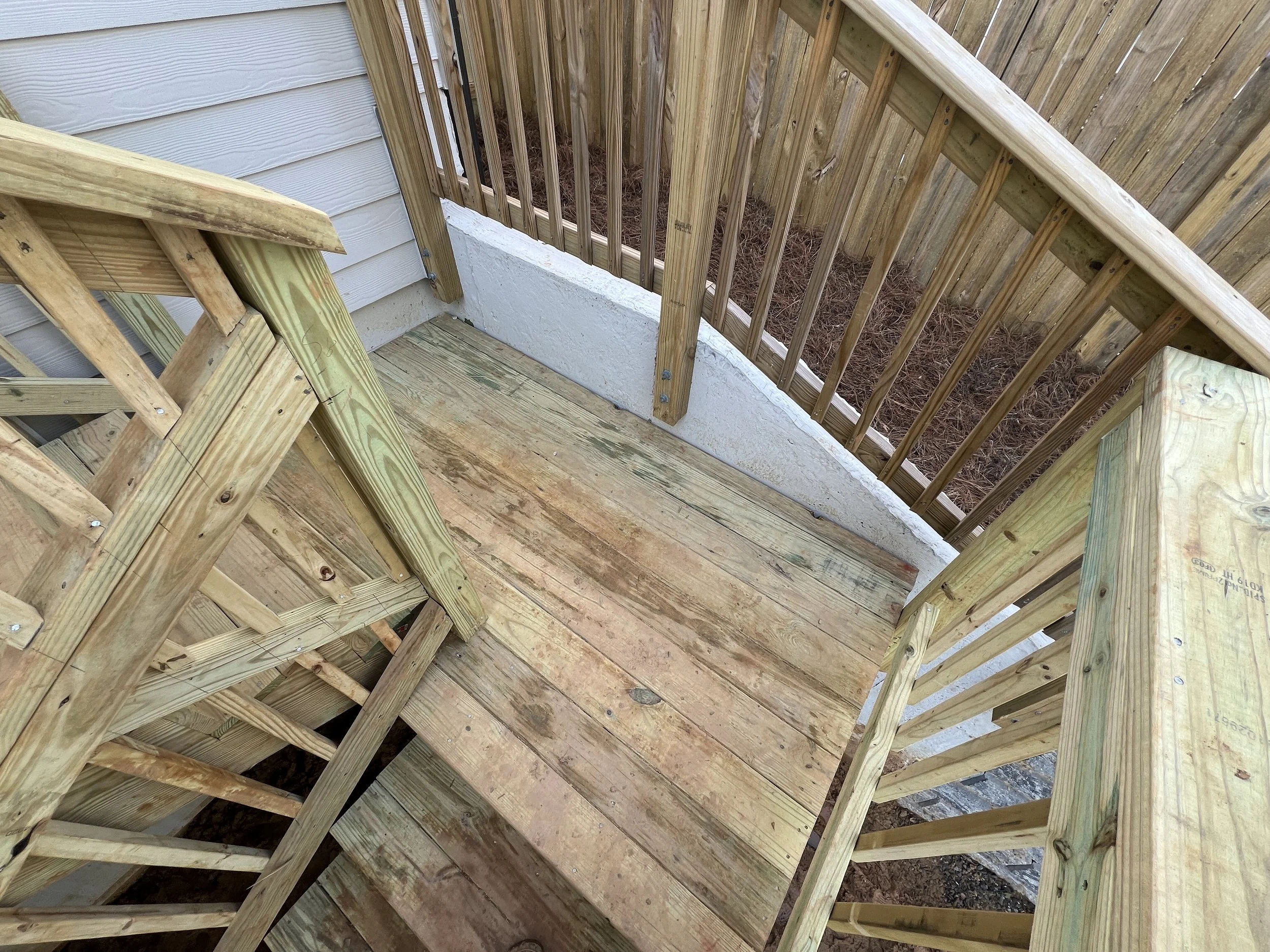View of a small wooden deck under construction, with unfinished wooden planks and a surrounding wooden railing.