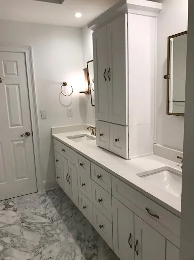 Bathroom with white cabinetry, marble floor, wall mirror, wall-mounted light, and a closed door.