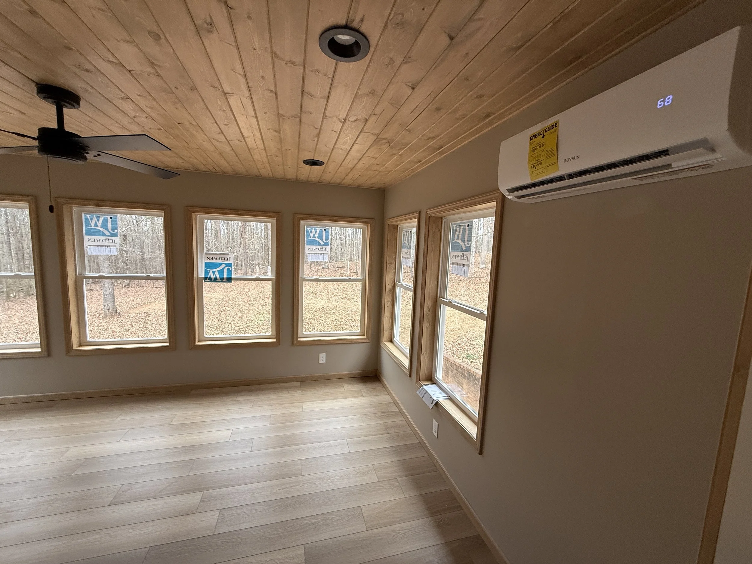 Interior of a room with a wood ceiling, multiple windows, a ceiling fan, and an air conditioning unit on the wall.