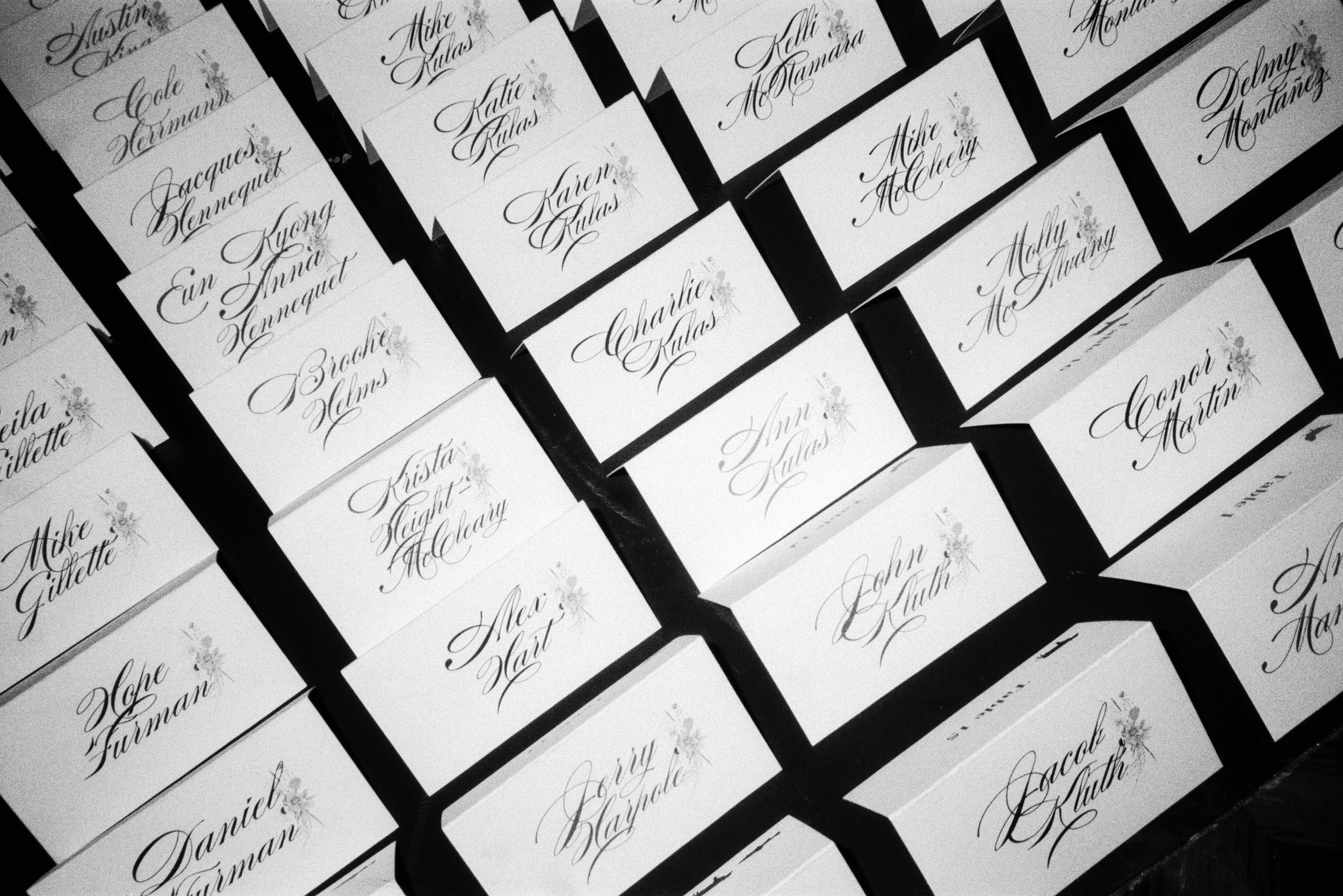 A black and white photograph of handwritten name cards arranged in multiple rows and columns, featuring elegant cursive calligraphy.