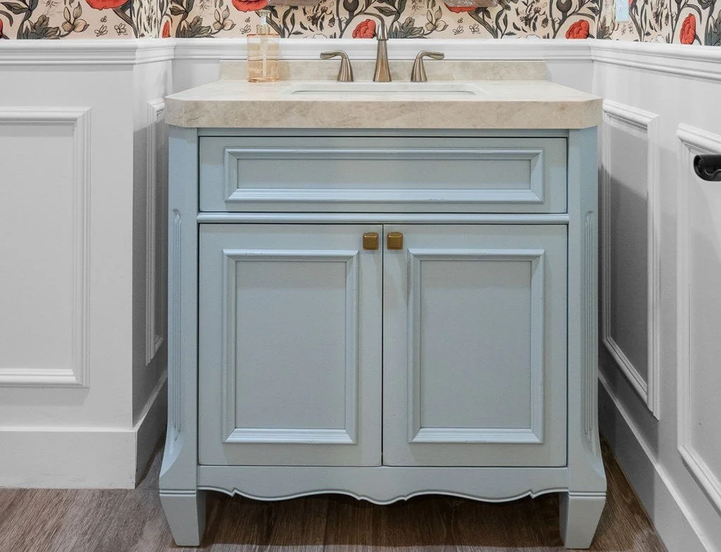 This custom bathroom vanity features Shiloh Custom Cabinetry painted in the striking Niebla Azul finish, complemented by sophisticated honey bronze hardware from Top Knobs. The combination of soft blue tones and warm metallic accents creates a refine