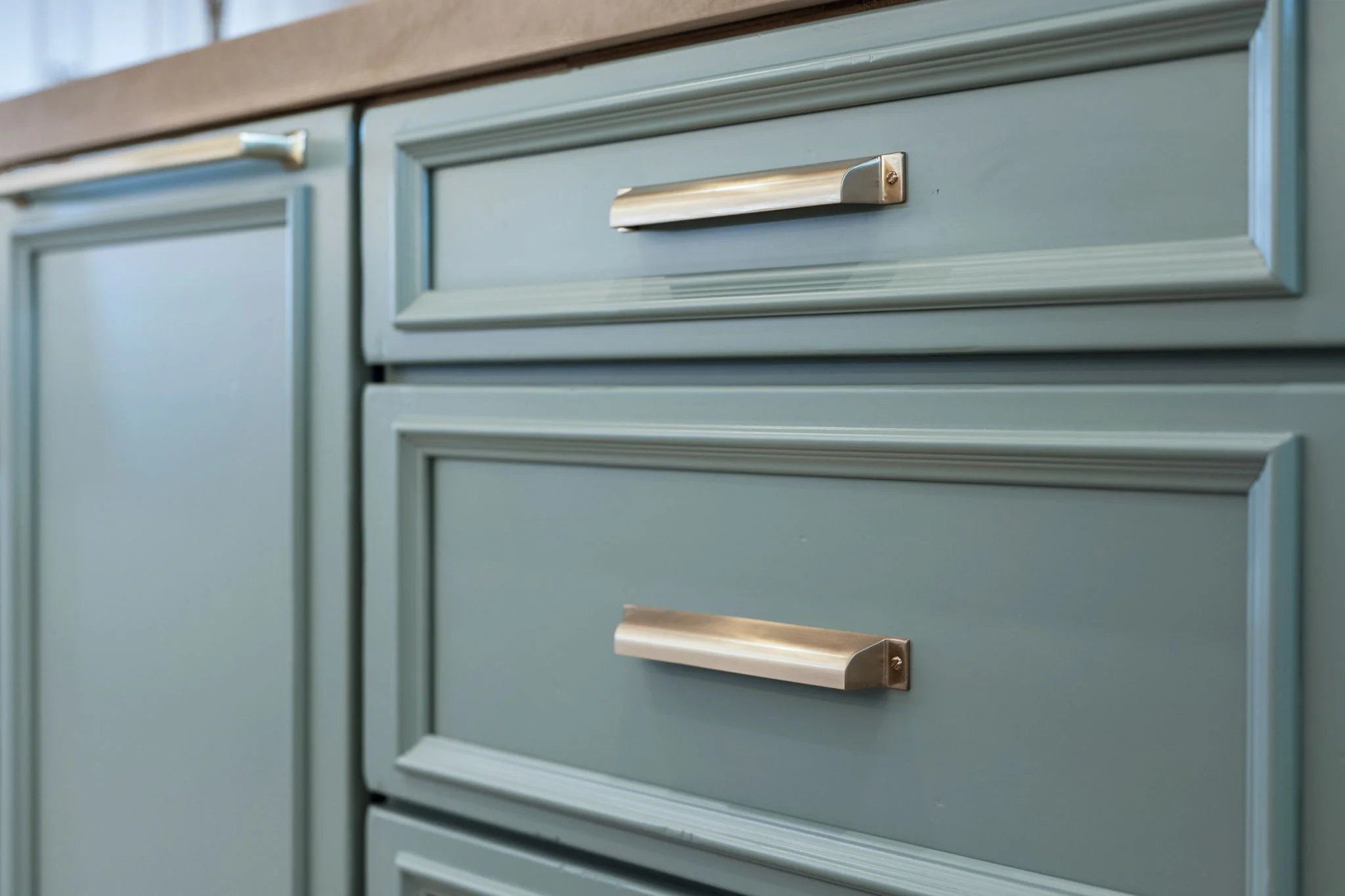 This custom kitchen island showcases Shiloh Custom Cabinetry painted in Evergreen Fog, a modern, nature-inspired color that adds depth and character to any space. Paired with honey bronze hardware from Top Knobs, this island serves as a bold focal po