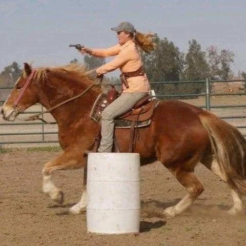 Woman riding a horse that appears to be shooting a gun while jumping over a barrel.