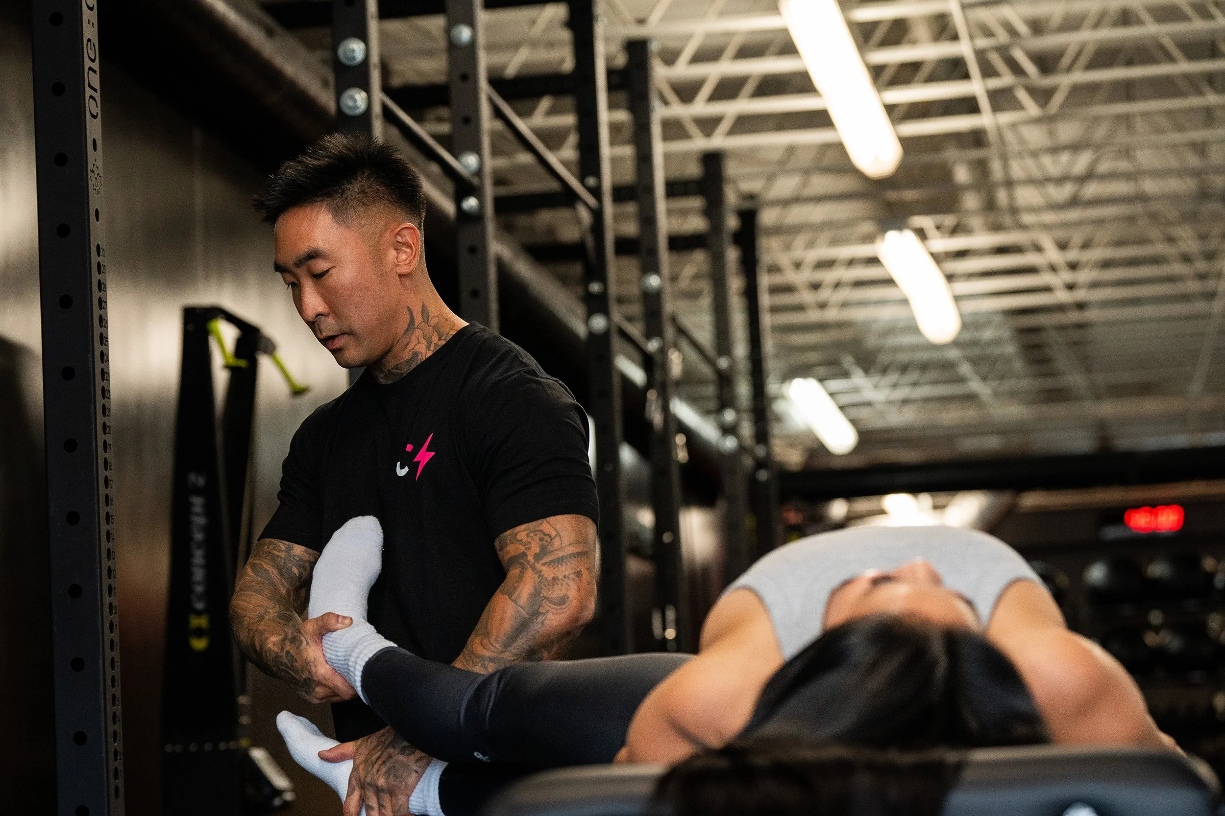 Fitness trainer assisting woman with leg exercise in gym.