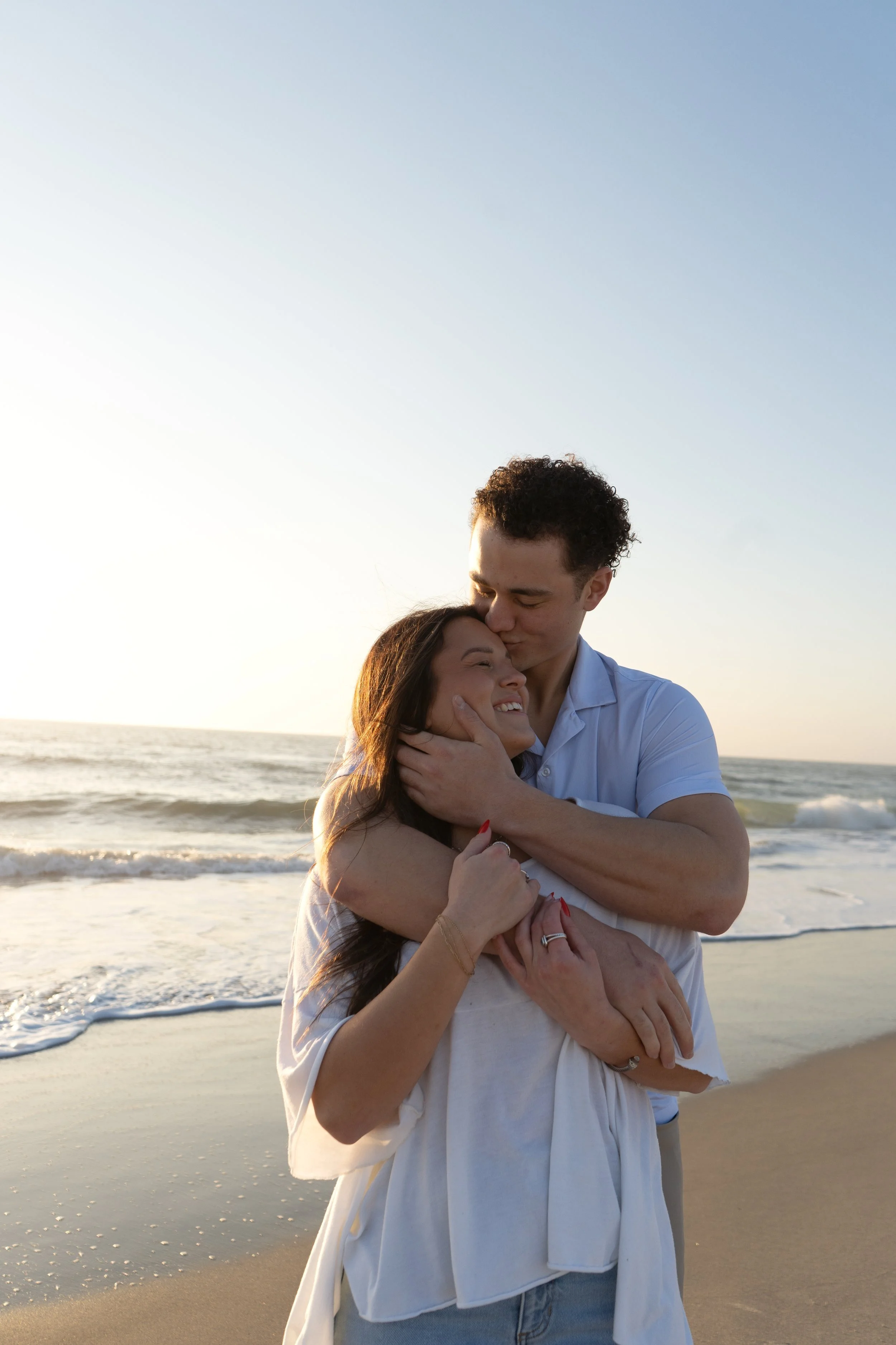 A happy couple embracing on a beach at sunset, with the ocean and sky in the background.