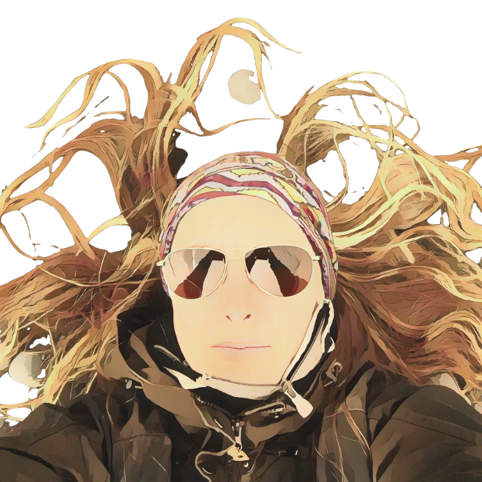 A person lying on the ground with long curly hair, wearing sunglasses, a colorful headscarf, and a black jacket, with their hair spread out around them.