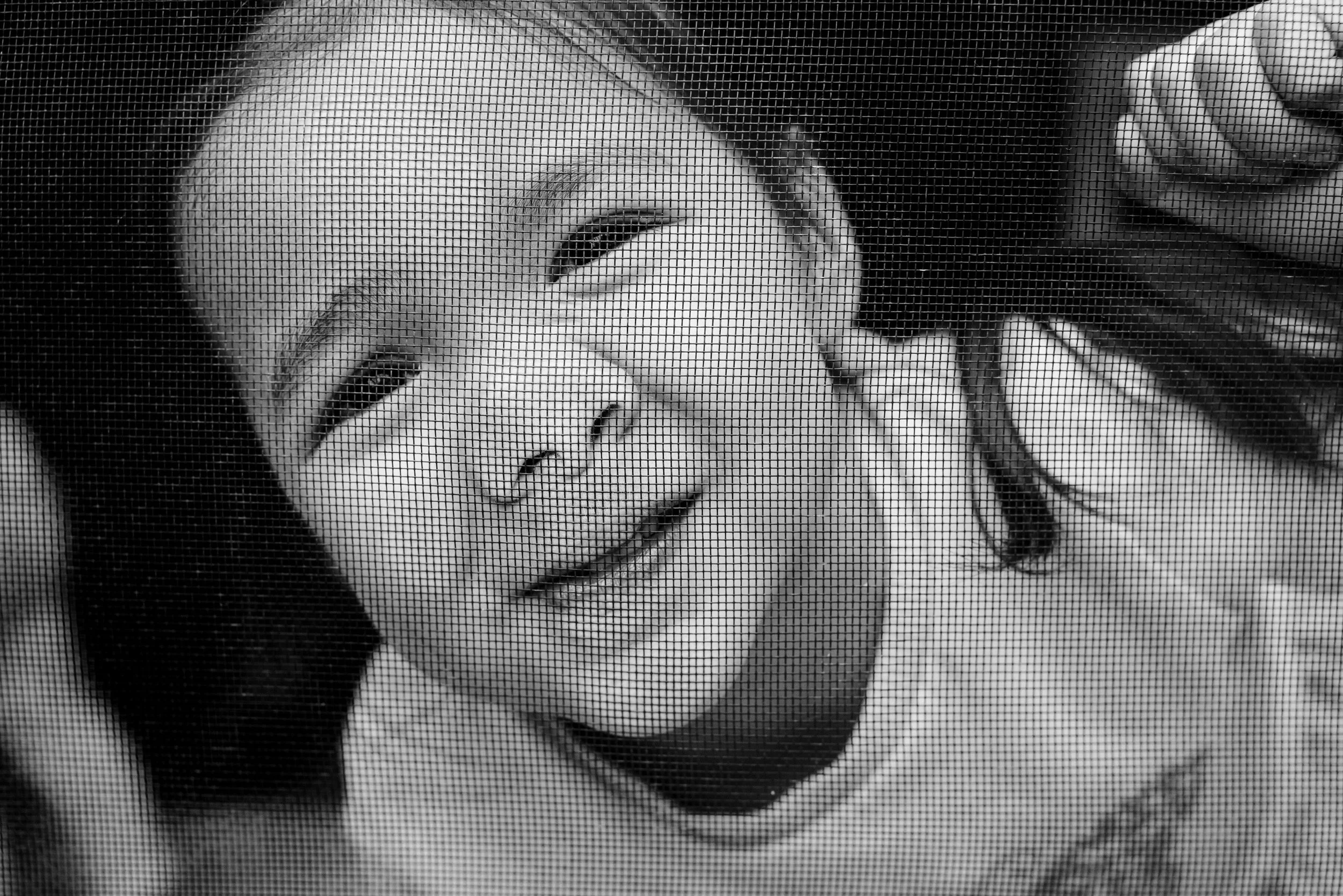 Close-up black and white photo of a girl's face, behind a window screen.