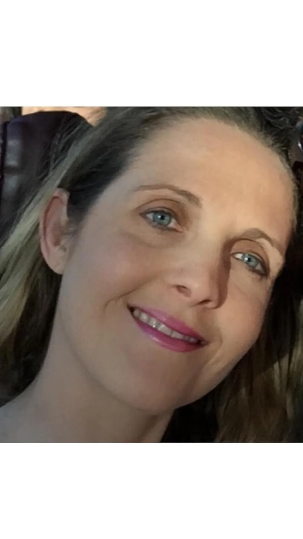 Close-up of a woman smiling with blue eyes and light makeup.
