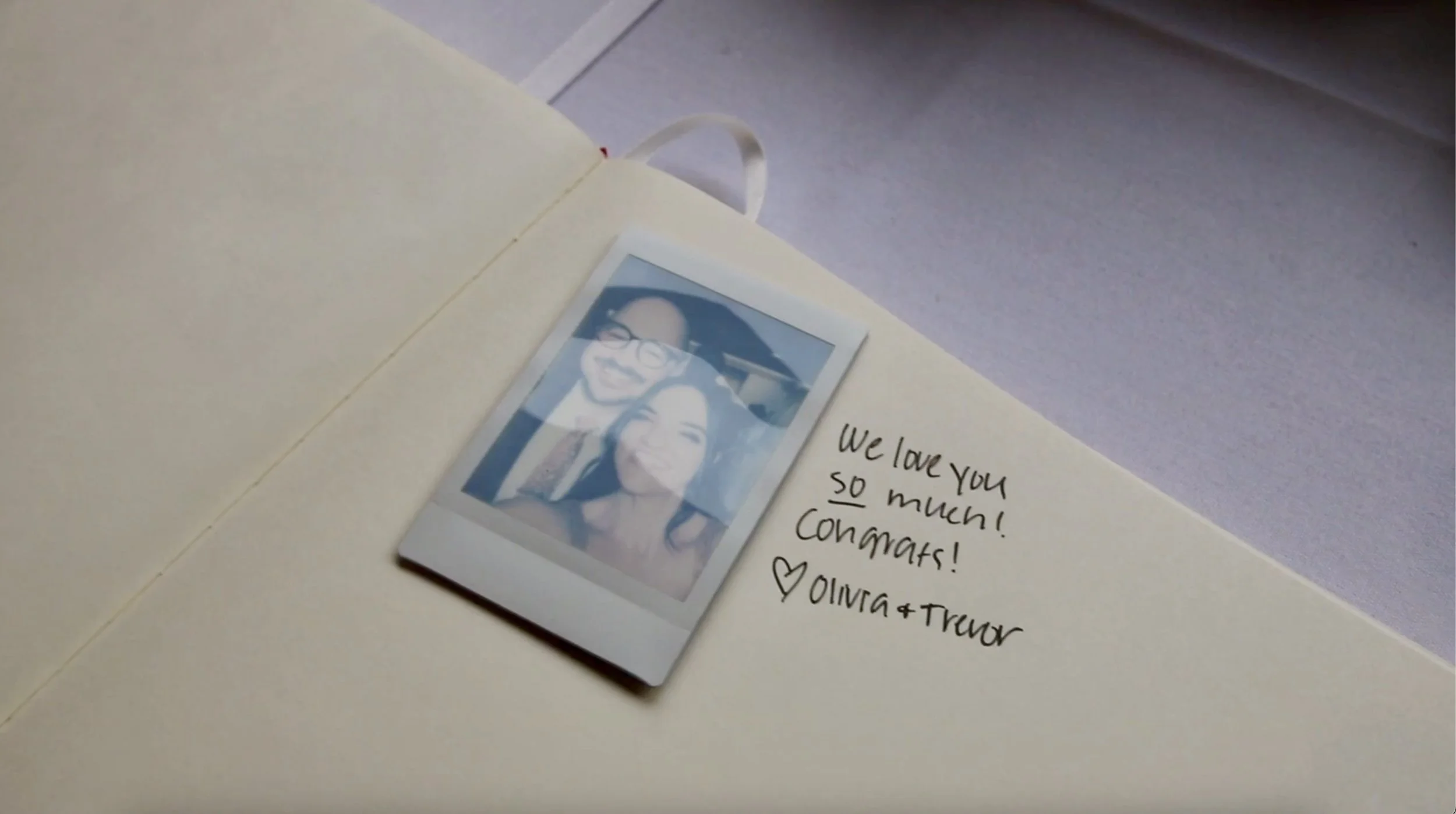 A photo of a polaroid picture of two women smiling, placed inside a greeting card. The card has a handwritten message that says, 'We love you so much! Congrats!