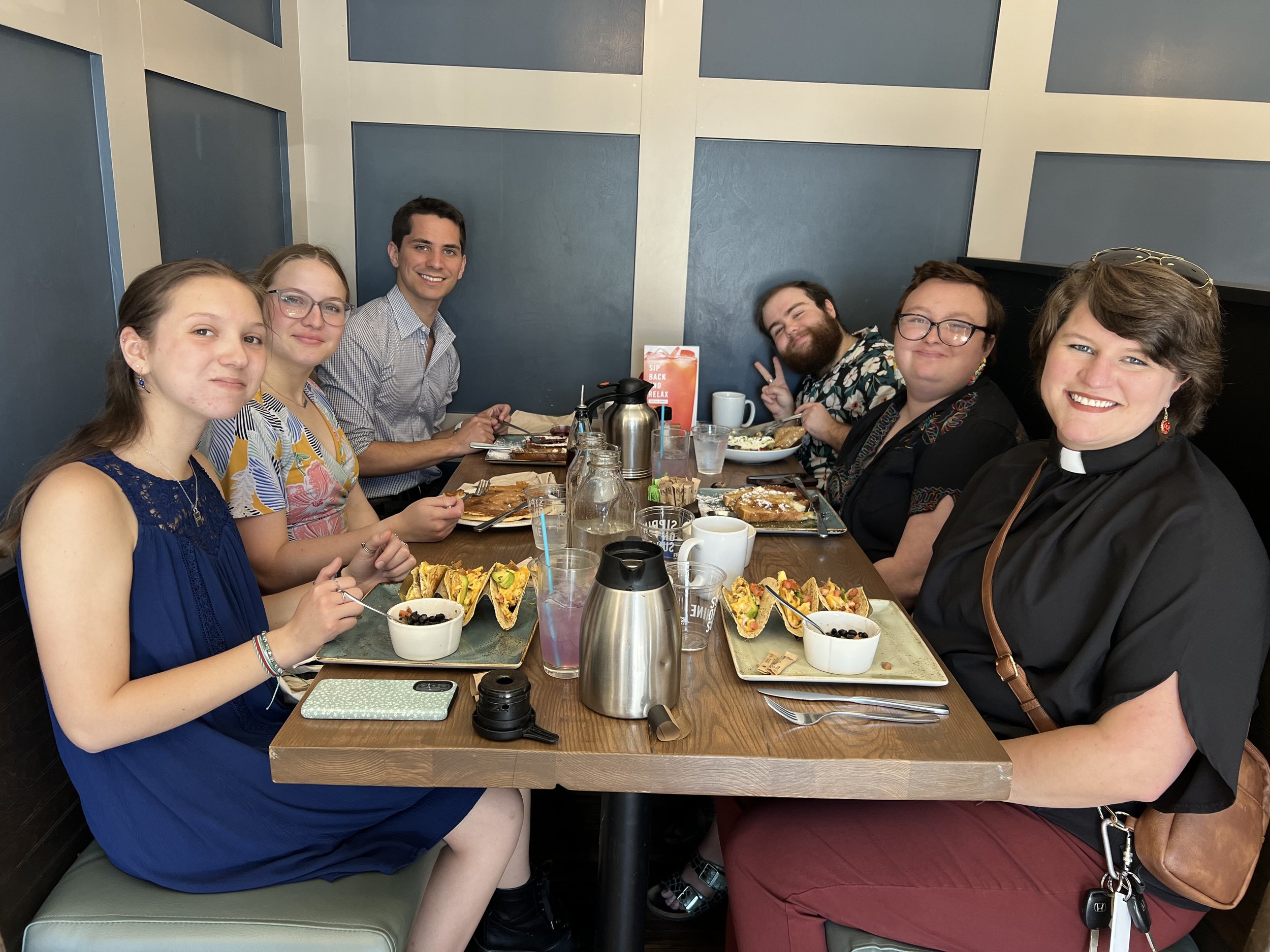 Group of people sitting at a dining table with food and drinks, smiling at the camera.