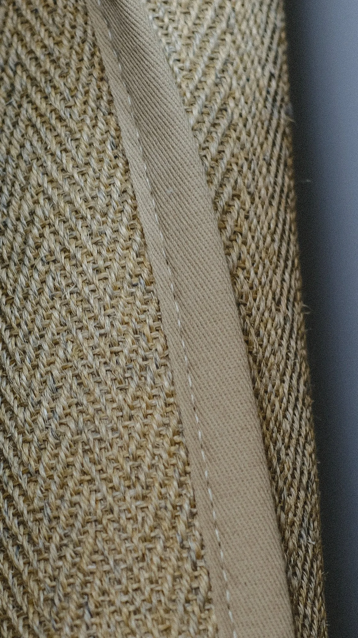 Close-up of a sisal carpet with a lighter beige seam or trim running vertically.