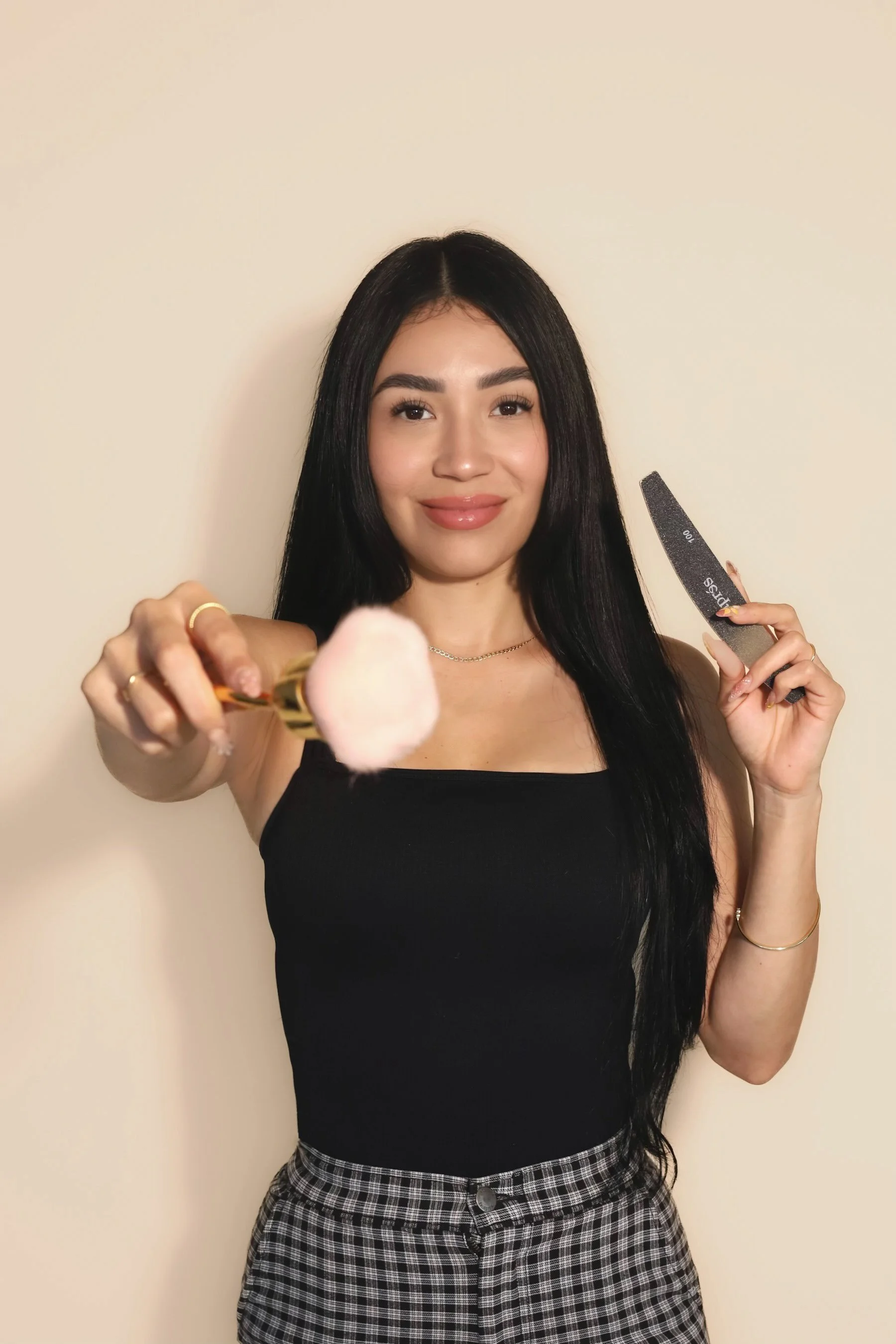 Portrait of a woman with long black hair, wearing a black top and a delicate necklace, standing against a dark background.