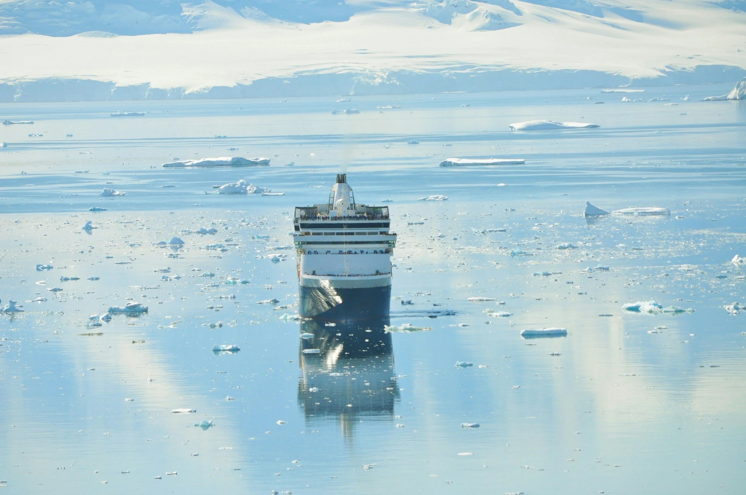 A large cruise ship navigating through icy waters surrounded by floating ice chunks and icebergs, with icy landscape in the background.