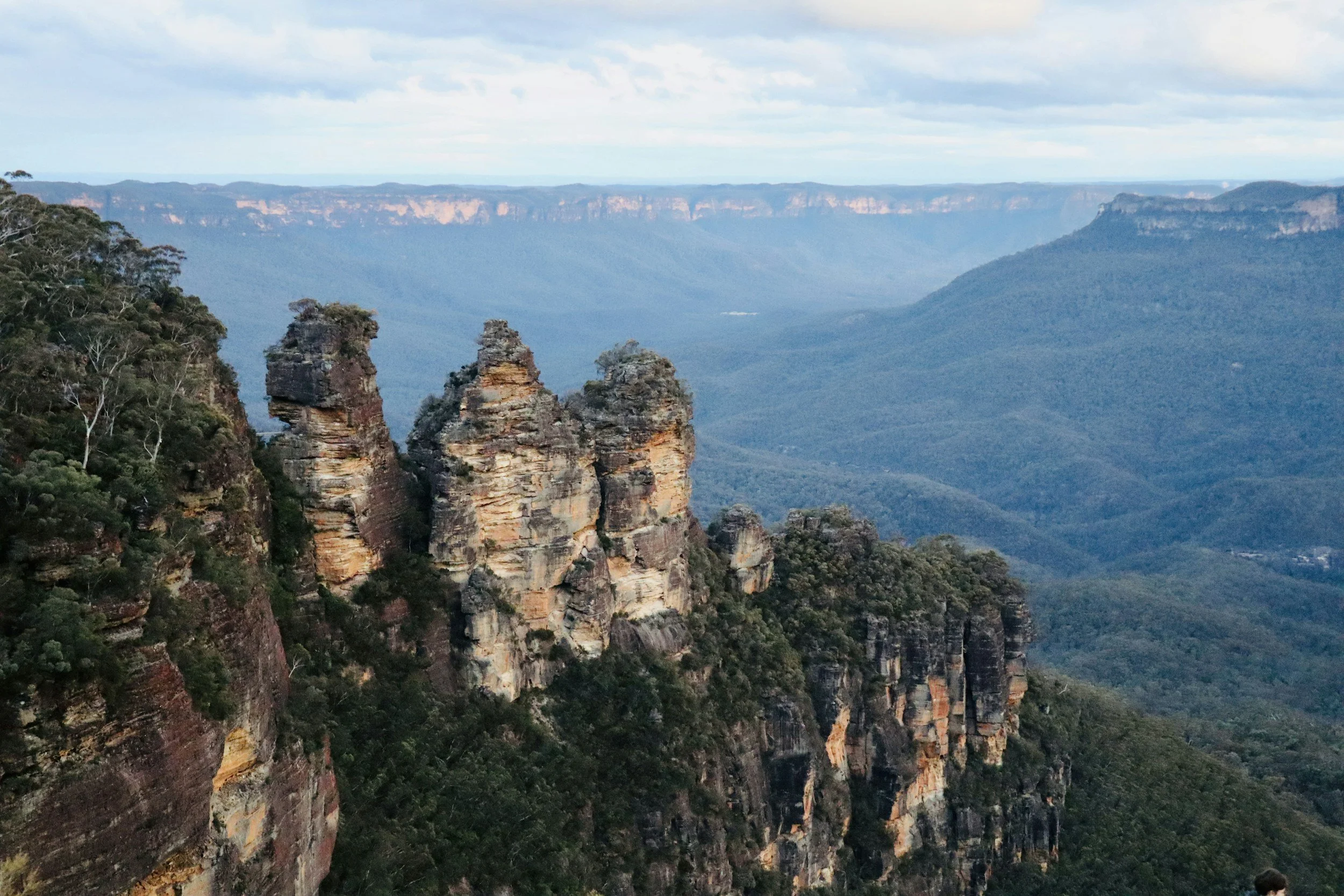 Cliffs and rock formations in the Blue Mountains with a forested valley background under a cloudy sky