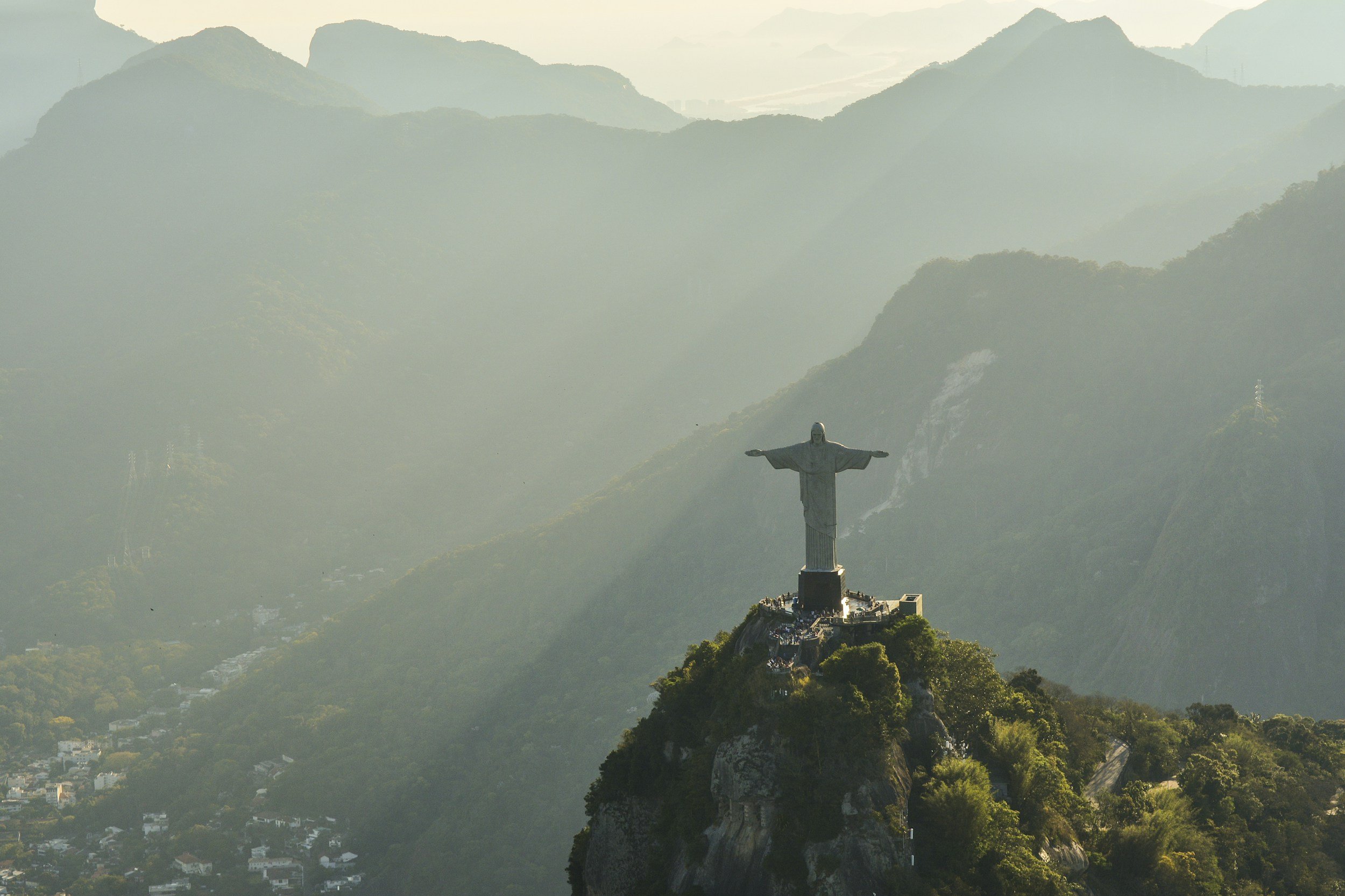 Statue of Christ the Redeemer with open arms on Corcovado Mountain overlooking Rio de Janeiro, Brazil, surrounded by misty mountains and a cityscape below.