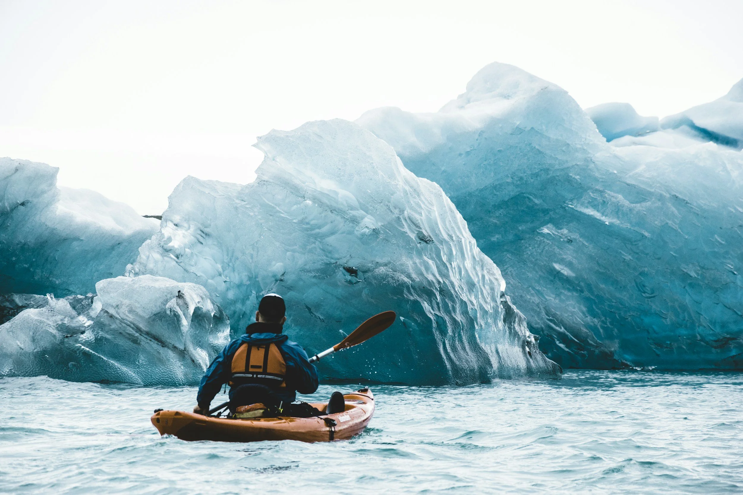 Person kayaking towards a glacier in icy waters.