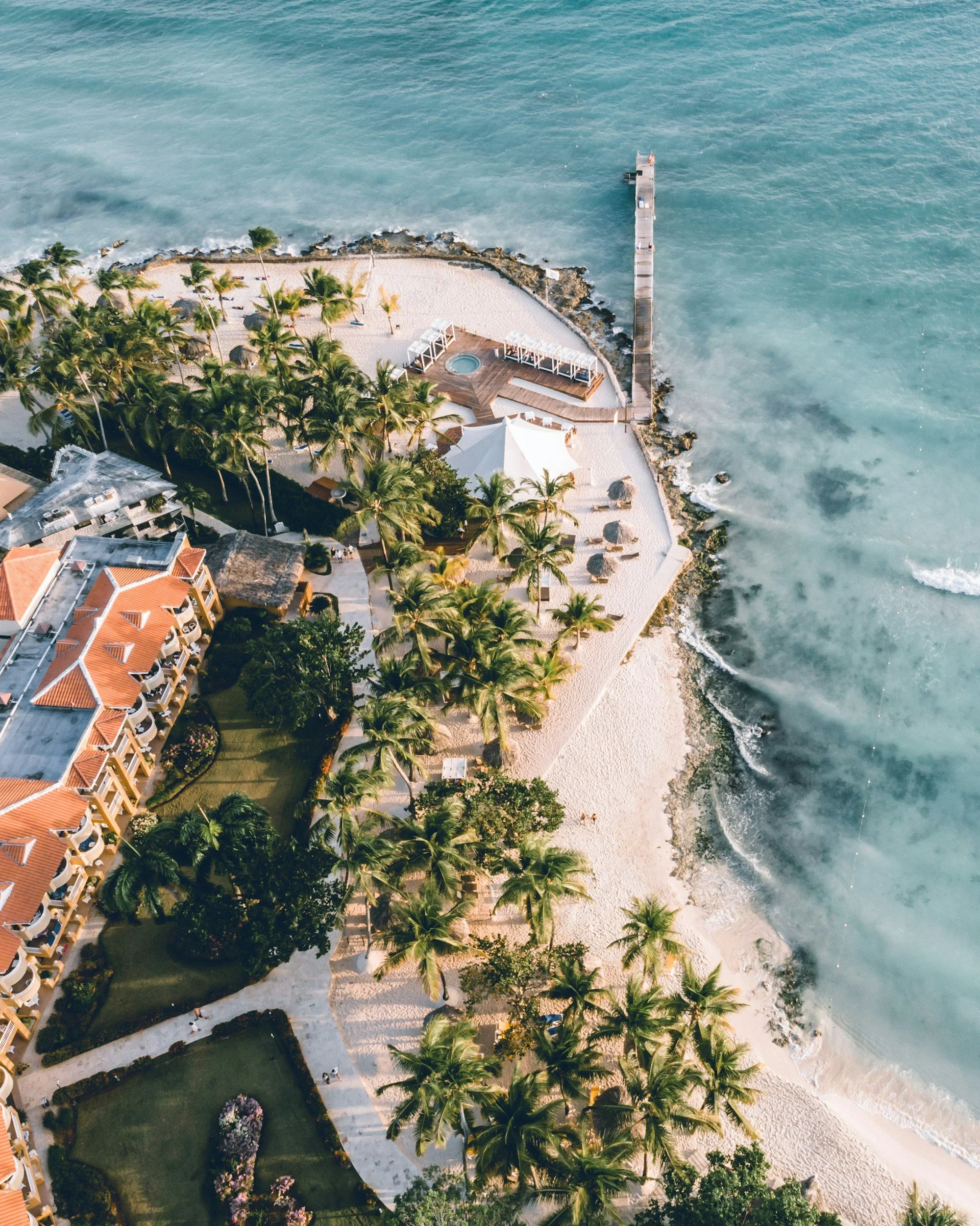 Aerial view of a tropical beach resort with palm trees, sandy beach, and ocean pier.