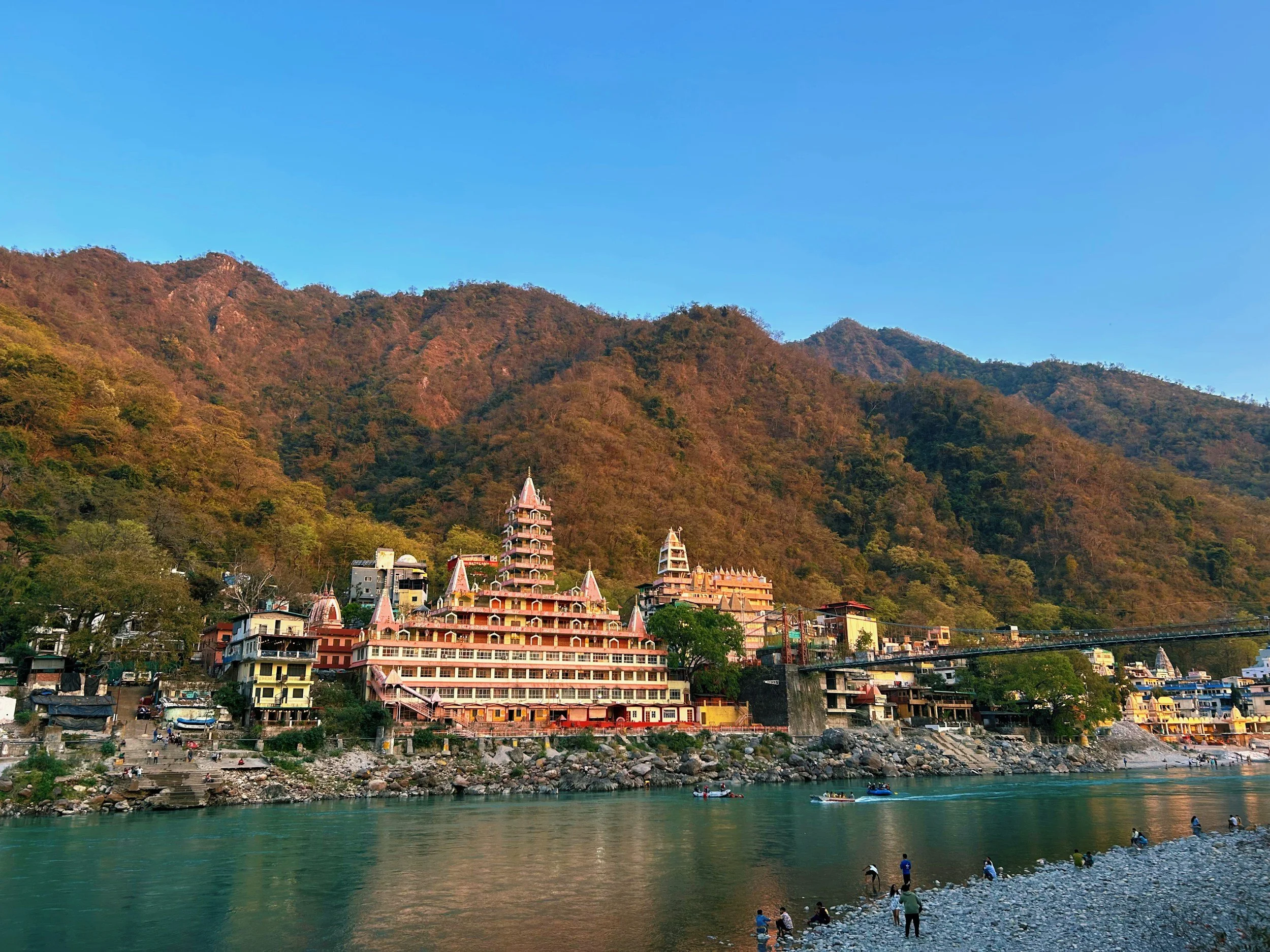 A colorful riverside town with buildings and temples at the foot of lush mountains during daytime.