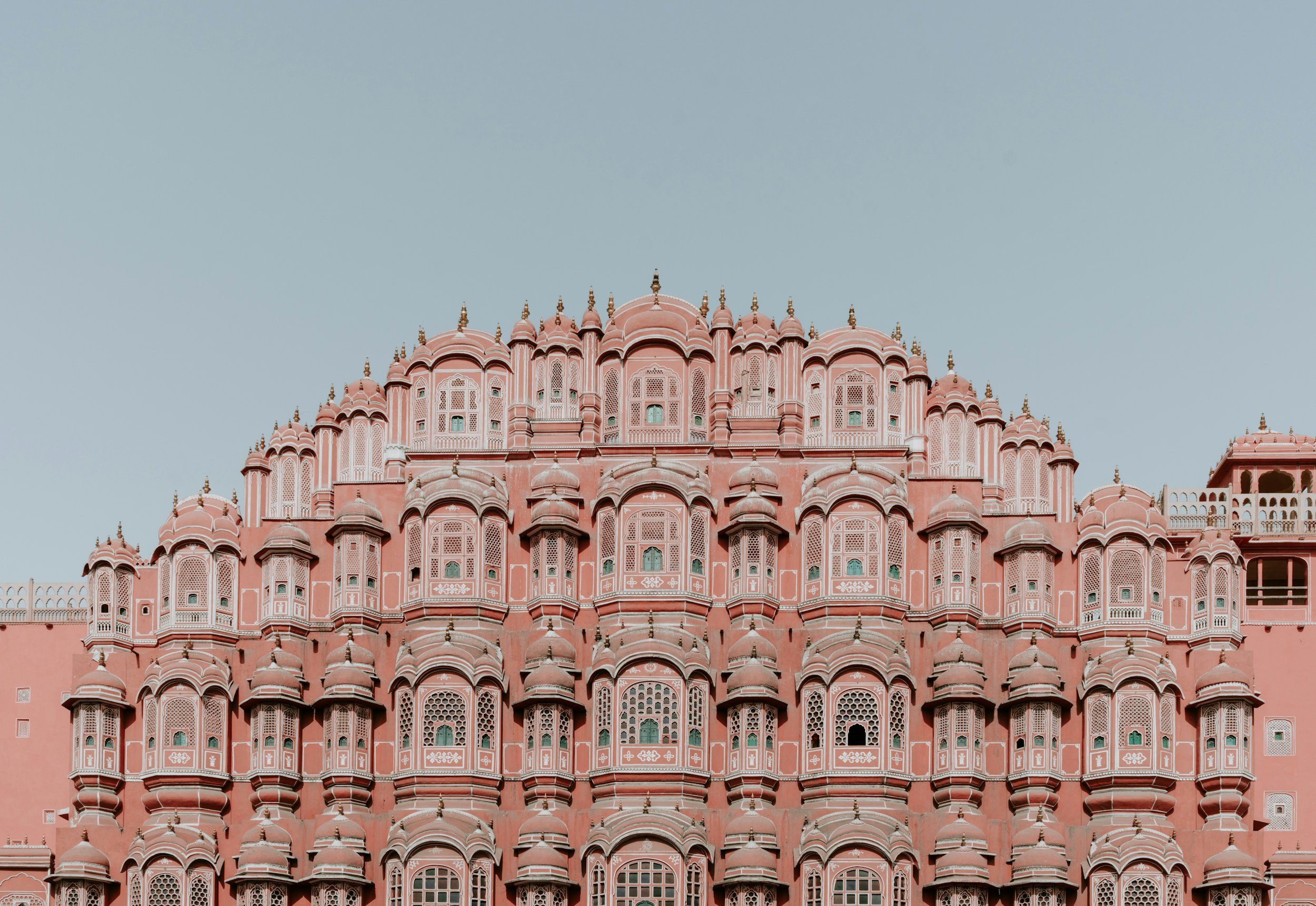 Pink historical palace with ornate architectural details and multiple domes and windows against a clear sky.