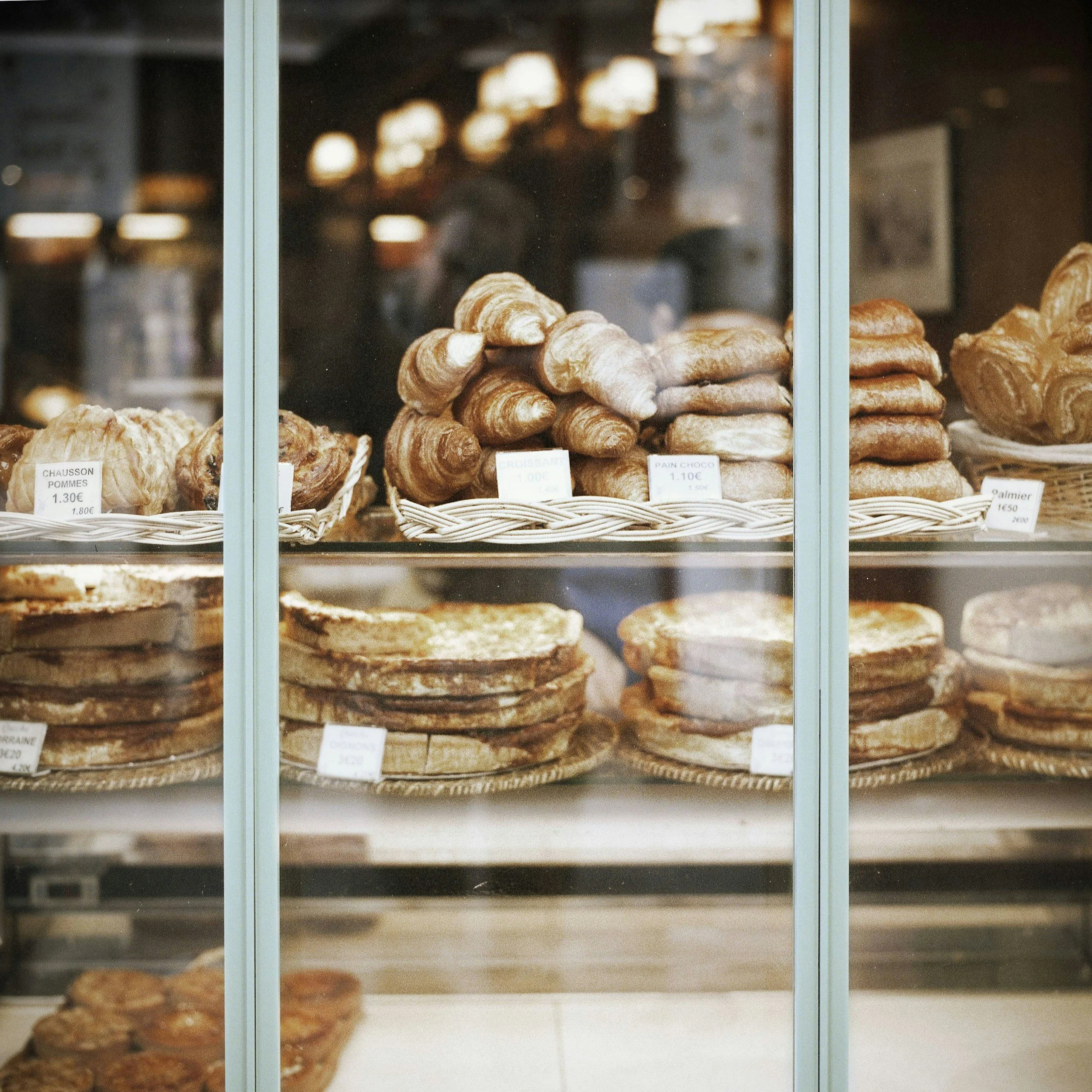 Display case with various baked goods, including croissants, pastries, and bread, labeled with prices.