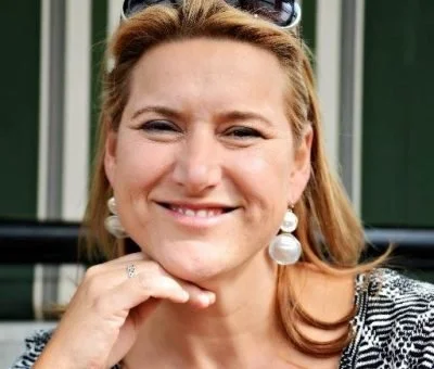 A woman with reddish hair and pearl earrings smiling outdoors.