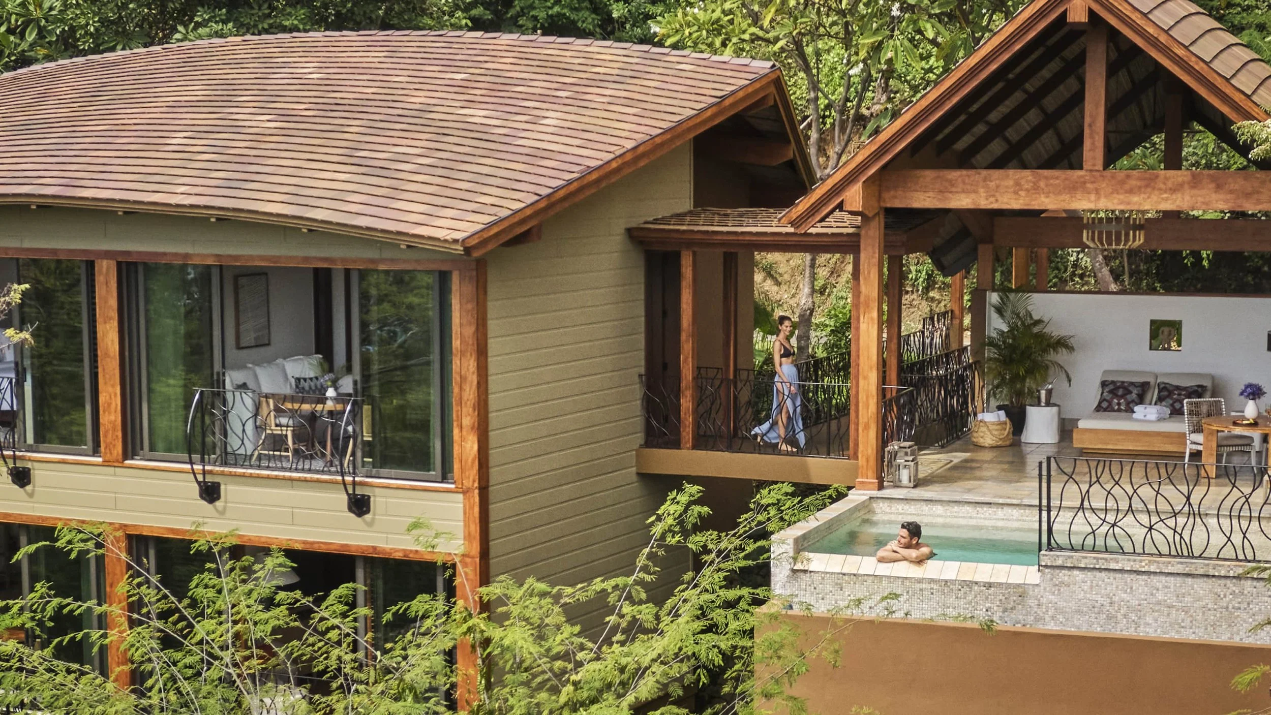 Luxury house with outdoor pool, sitting area, and large windows, surrounded by trees.