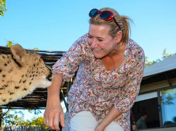 Woman smiling at a cheetah outdoors on a sunny day.