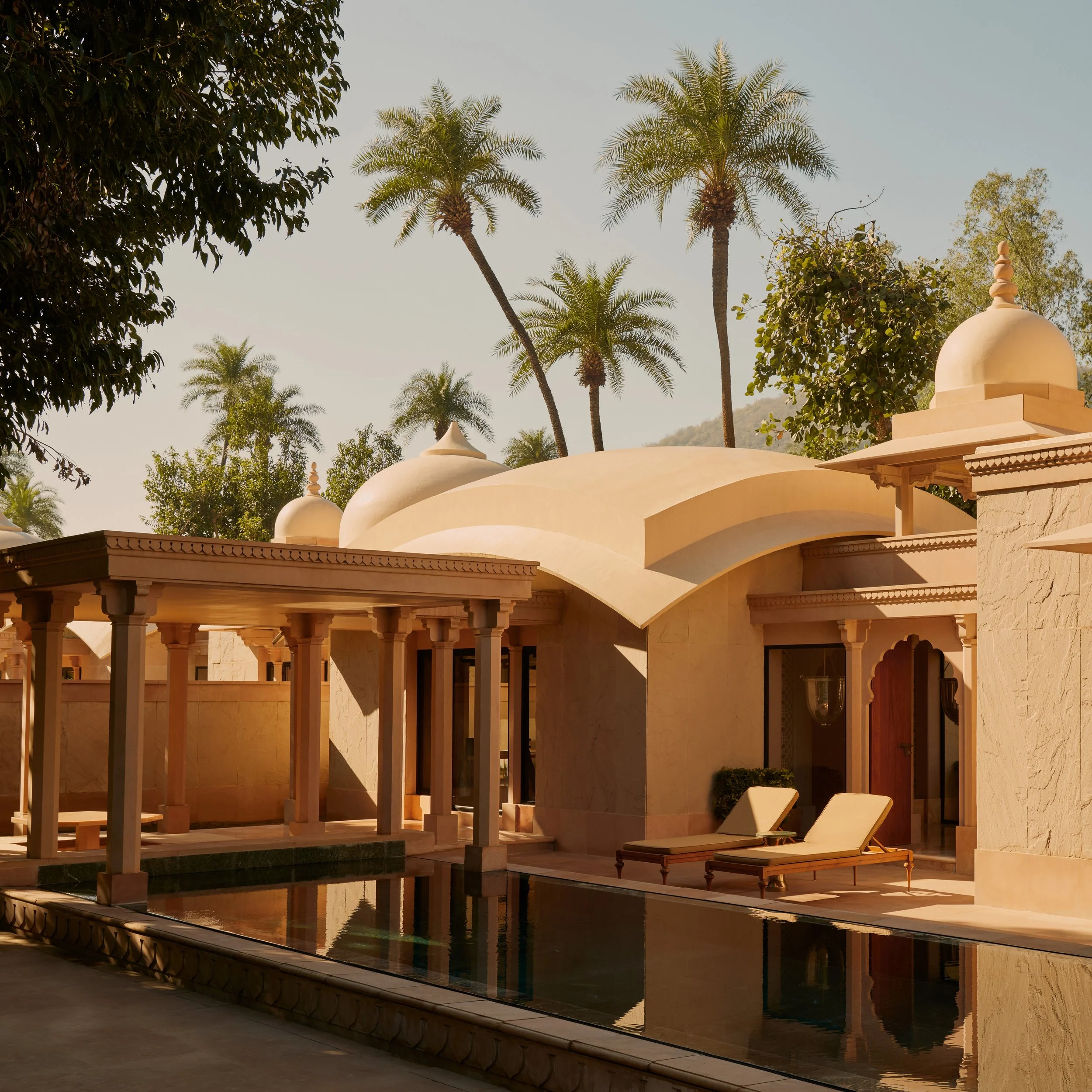 Luxury beige villa with domed rooftops, surrounded by palm trees, featuring a pool and sun loungers.