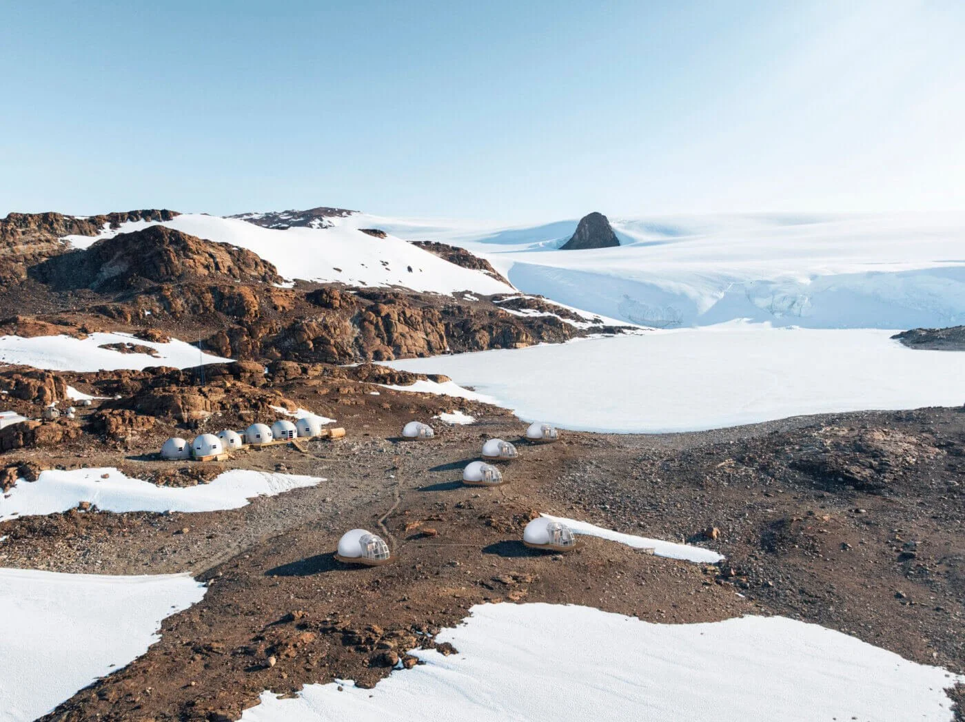 A scientific research station with white dome-shaped buildings in a snowy, mountainous landscape during daytime.