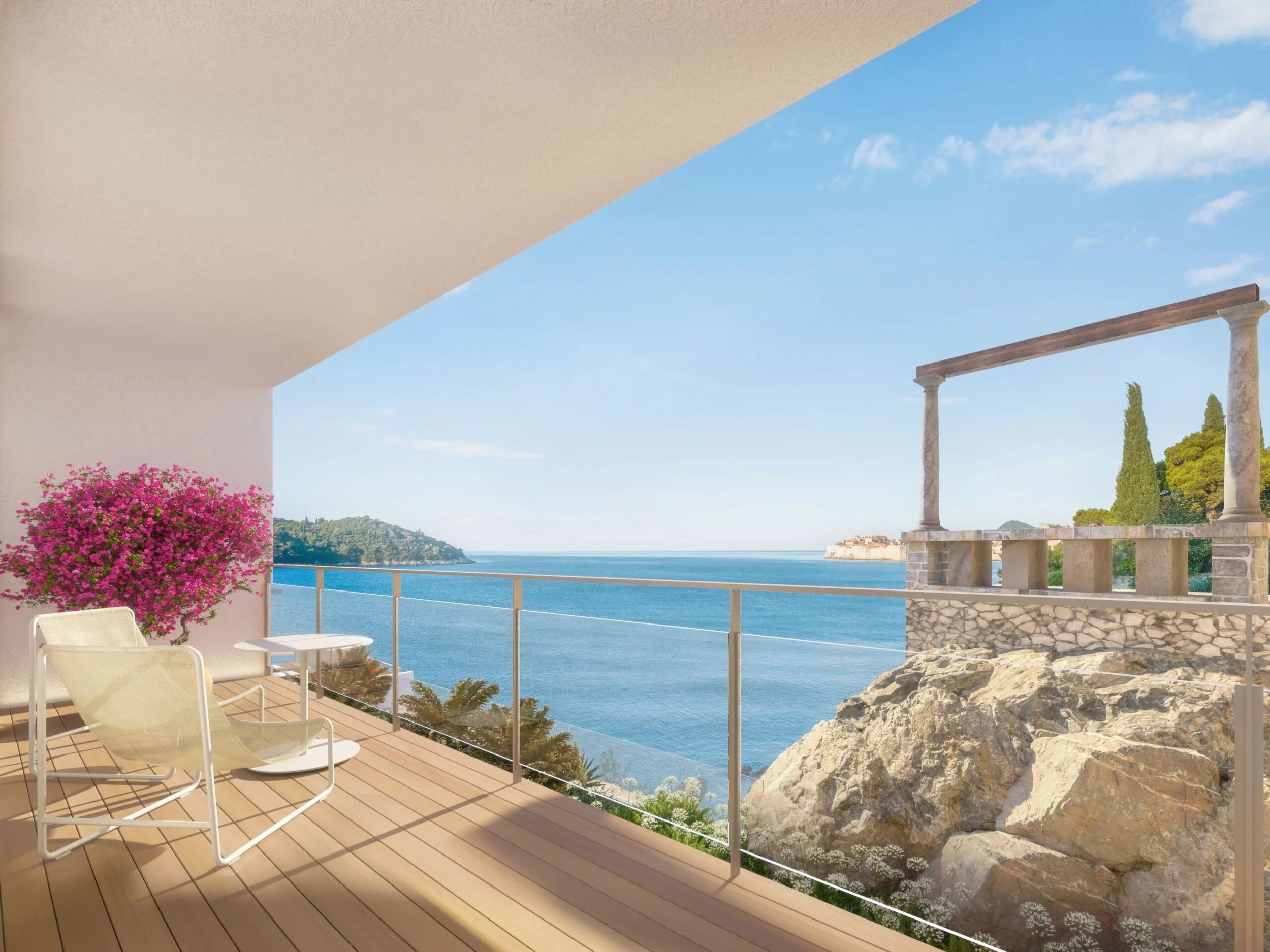 Balcony view overlooking ocean, rocky coastline, and distant land with trees, with a white chair, matching table, and pink flowering plant on a wooden deck.