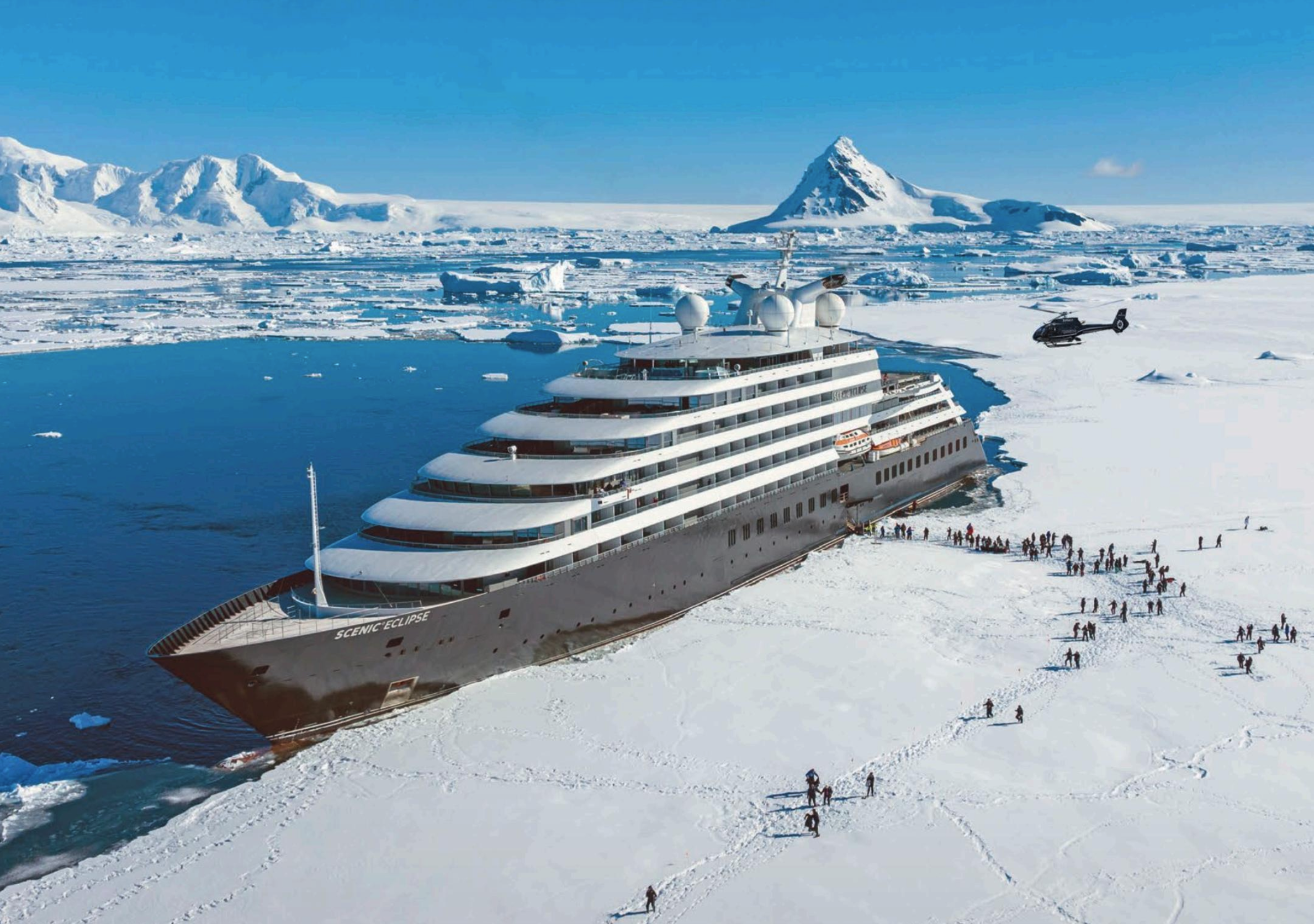 A large cruise ship named Scenic Eclipse stranded in ice and snow in a polar region, with a helicopter on the ice nearby and numerous people walking nearby.