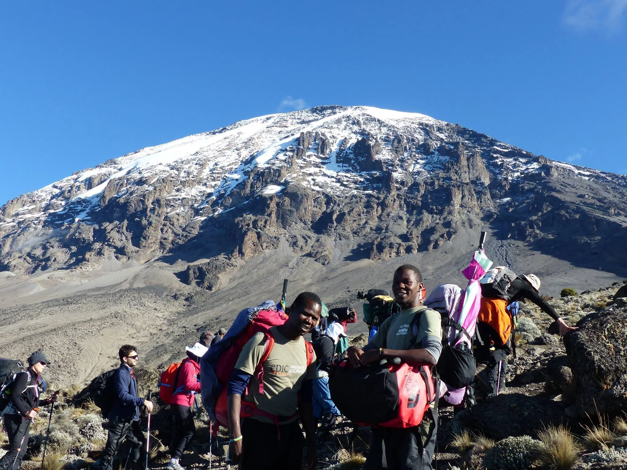 Group of hikers standing on rocky terrain with Mount Kilimanjaro in the background.