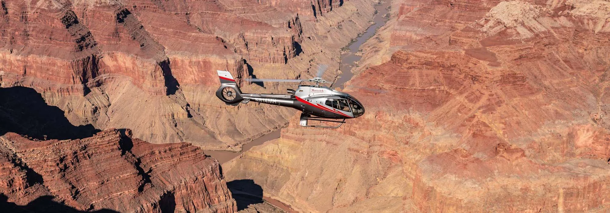 A helicopter flying over the Grand Canyon with the Colorado River visible below.