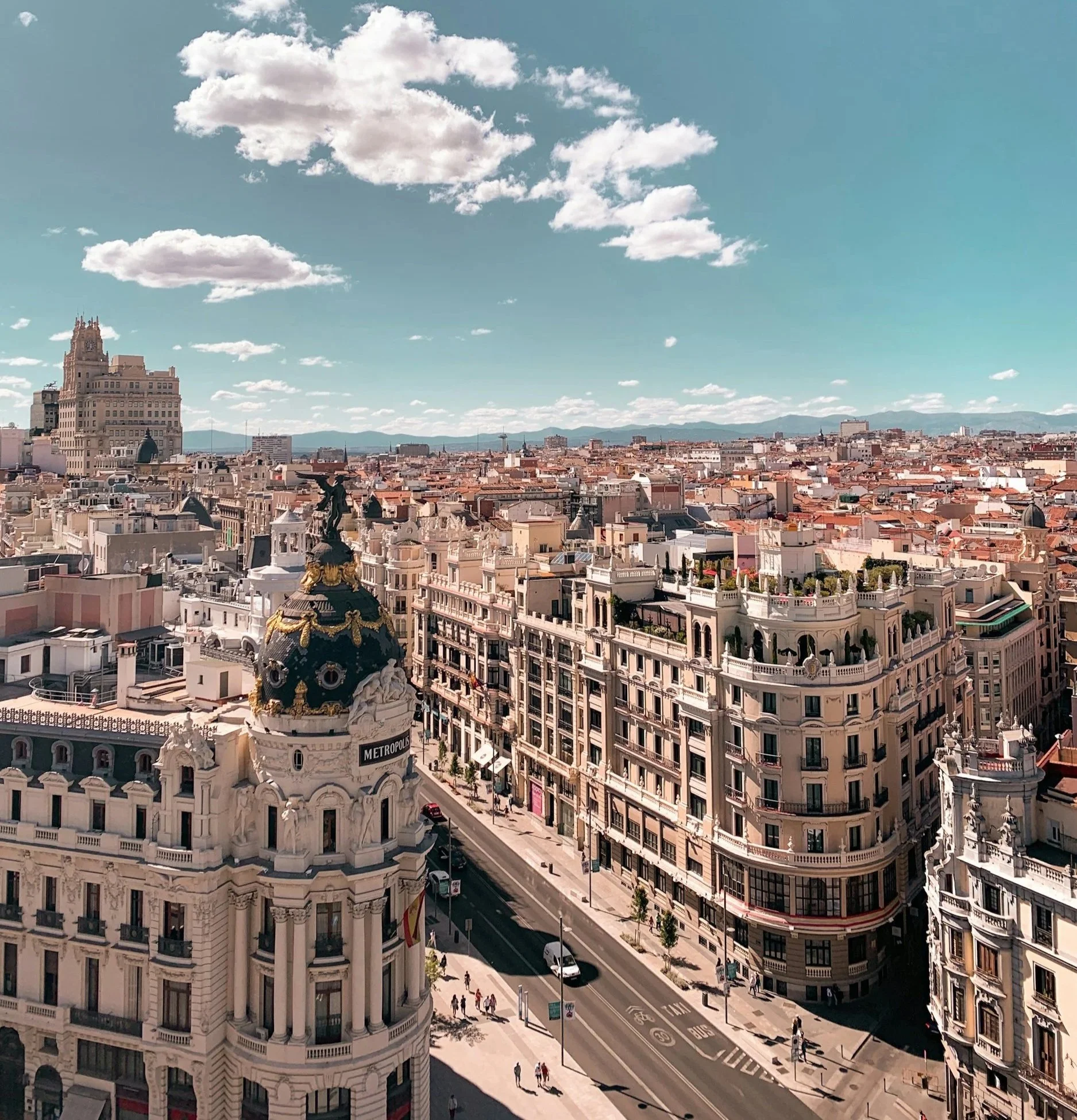 A city skyline with historic and modern buildings, including a domed building with a statue on top, under a partly cloudy sky.