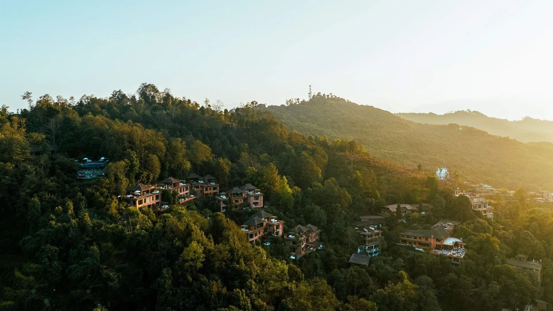 Houses on a lush green hillside with a mountain in the background, sunlight casting a warm glow.