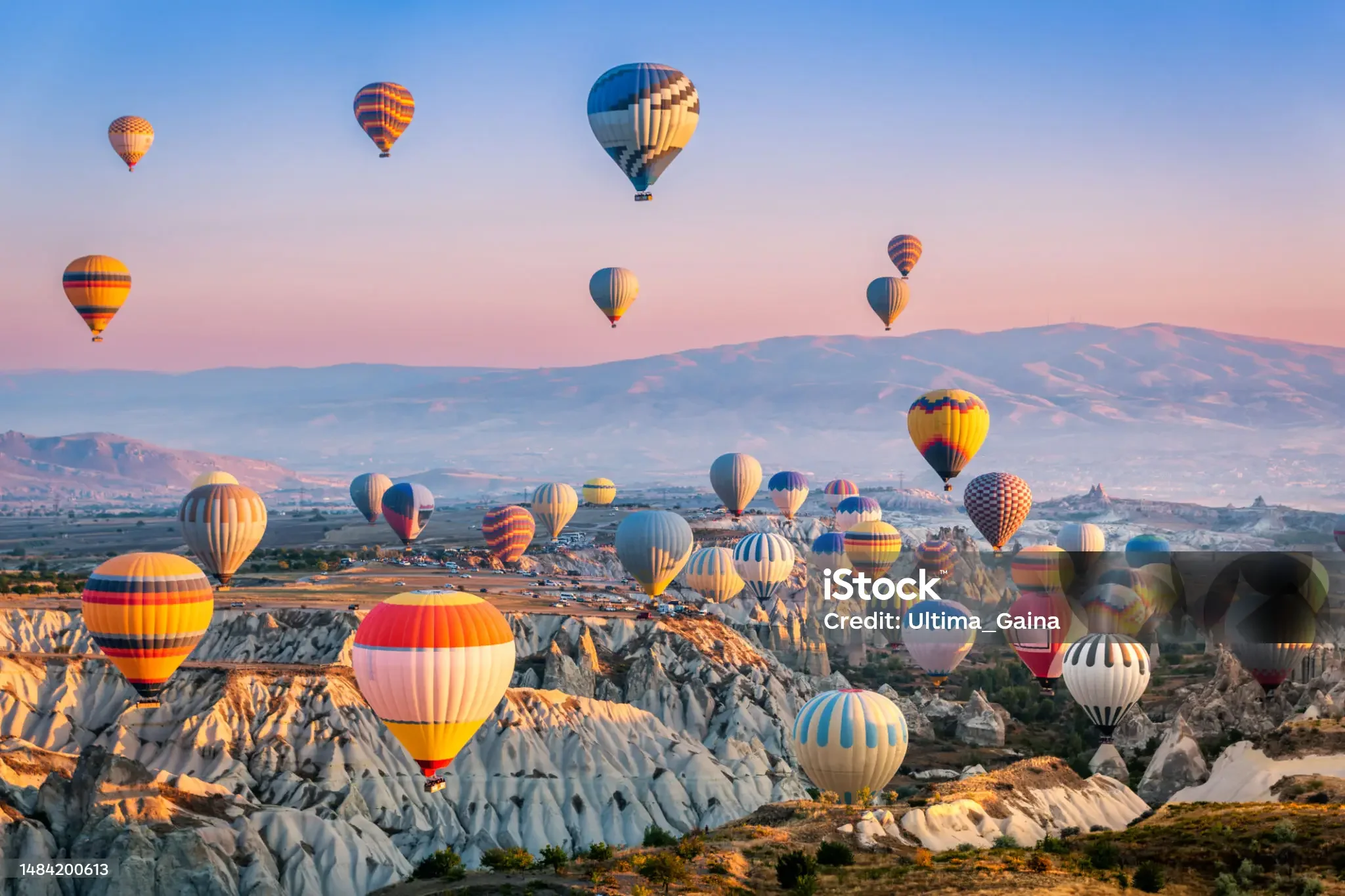 Multiple hot air balloons floating in the sky above a rocky, mountainous landscape during sunrise or sunset.