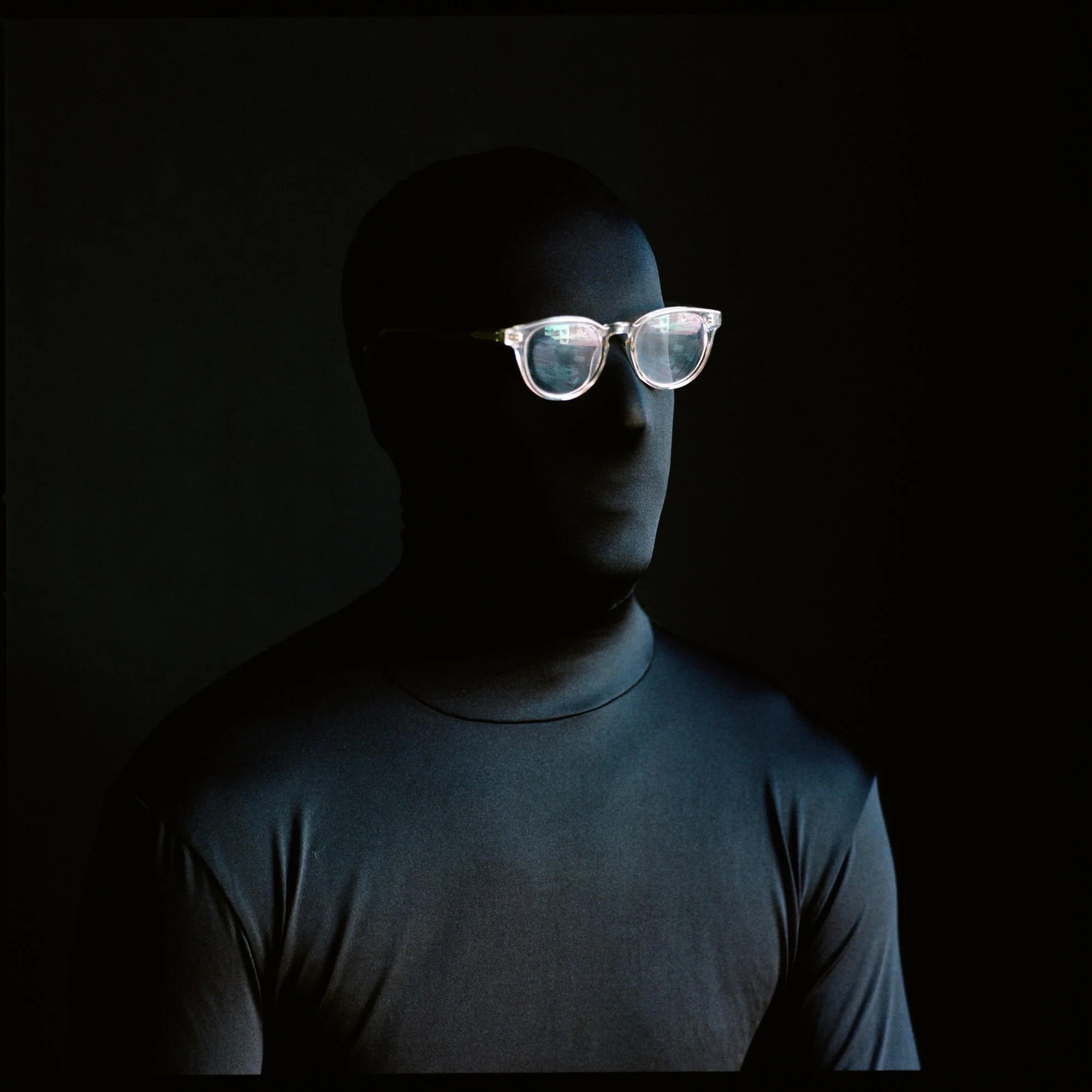 Man wearing reflective glasses and a dark shirt, with a dark background.